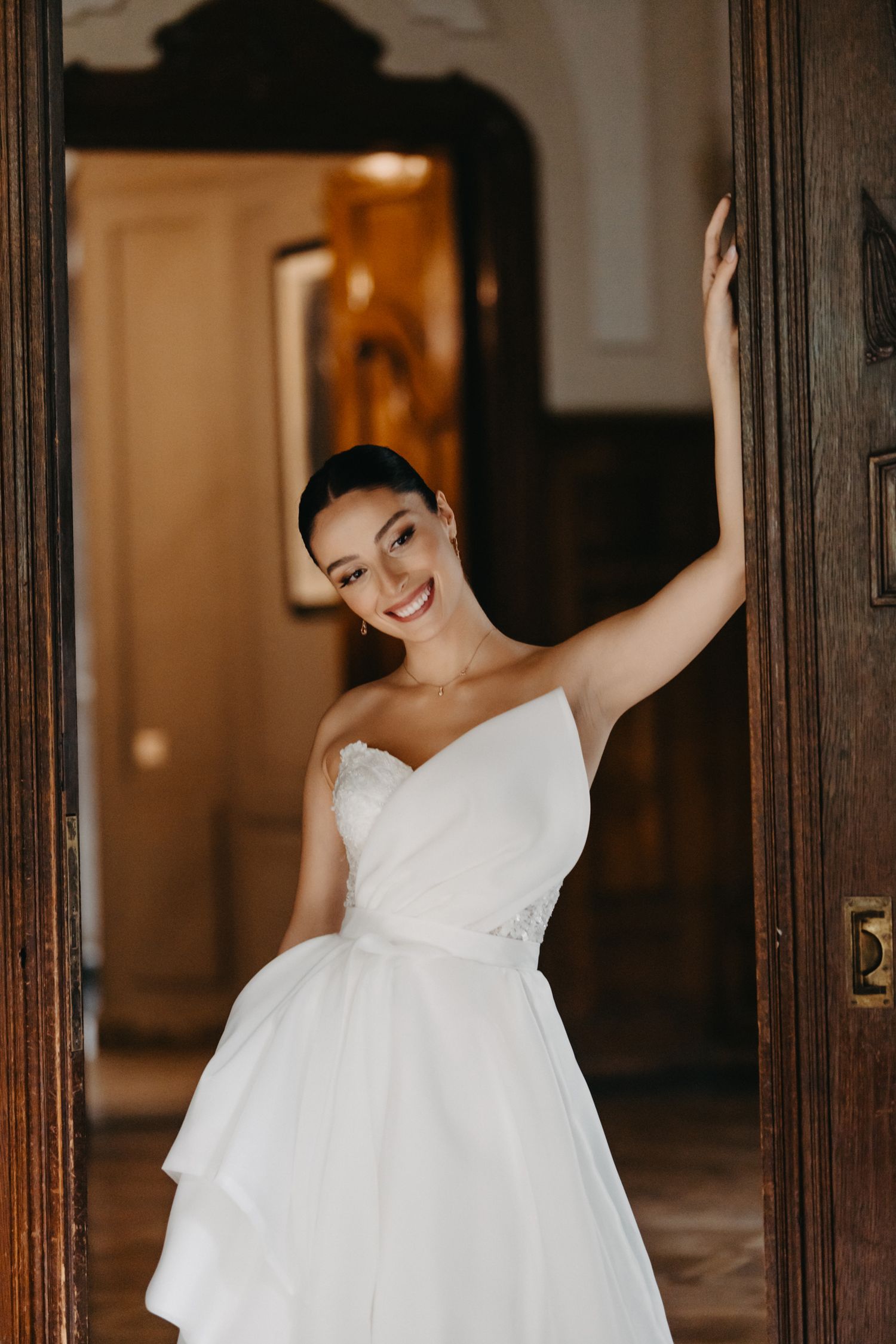 Joyful moments captured of bride in white dress posing against wooden doorframe.
