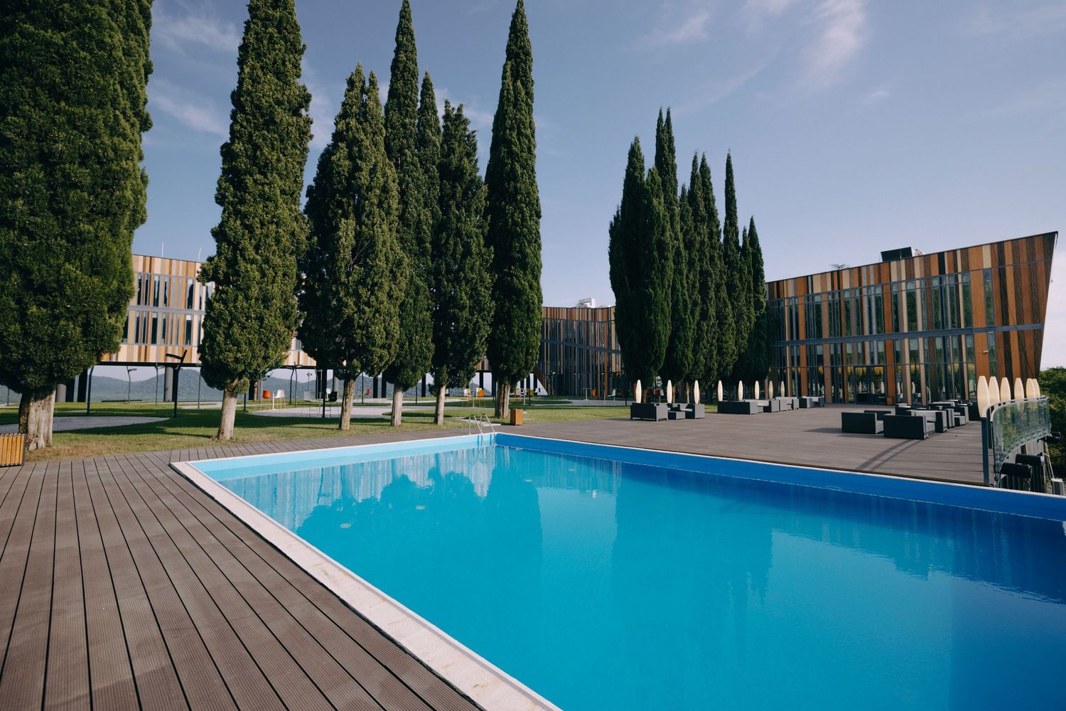 Modern architectural complex with swimming pool, cypress trees, and curved landscaping elements.