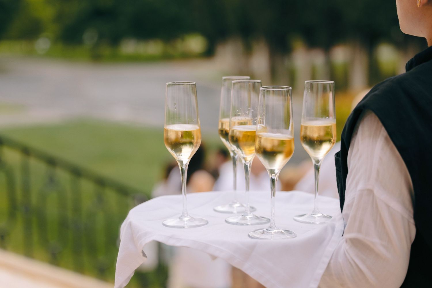 Champagne glasses being served on silver trays at an elegant outdoor event.