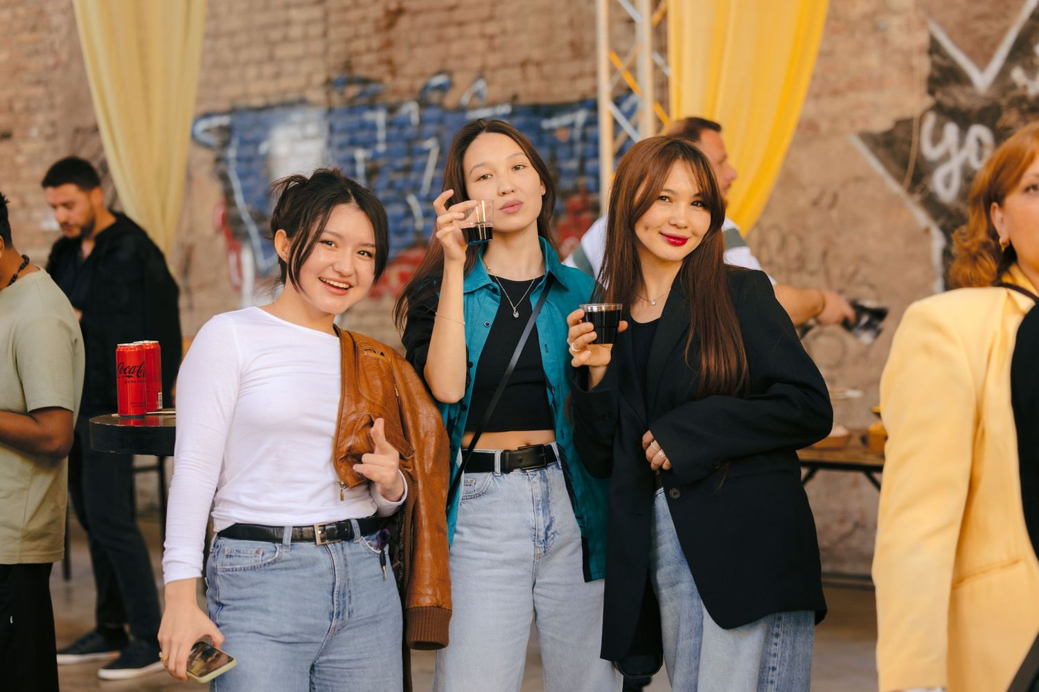 People mingling at a social gathering with brick walls and yellow curtains in the background.