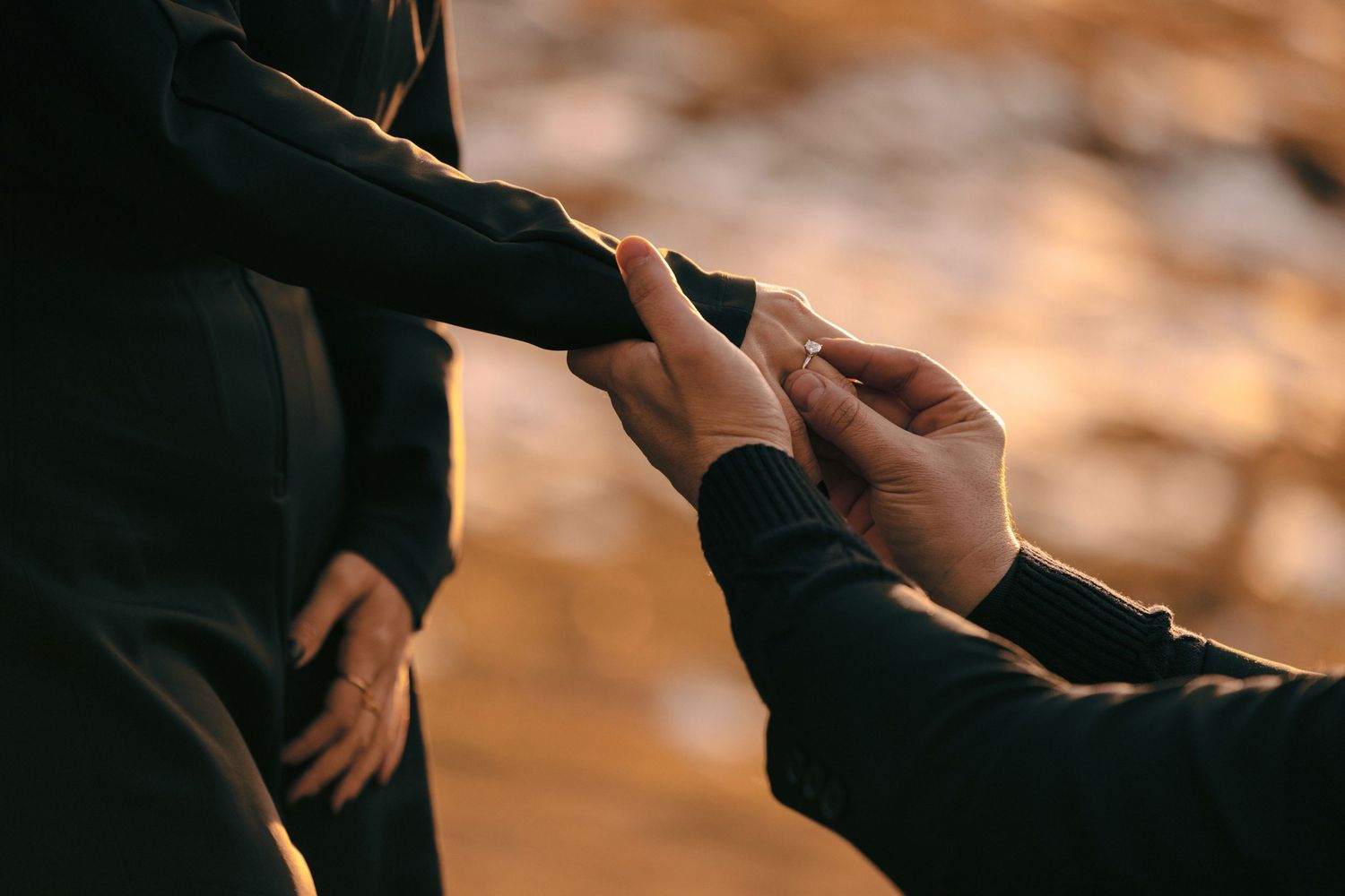 Close-up shot of hands during a romantic mountain proposal at golden hour.
