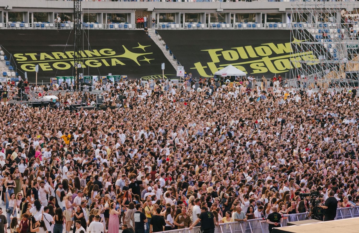Massive crowd fills stadium stands with large banner display visible above.