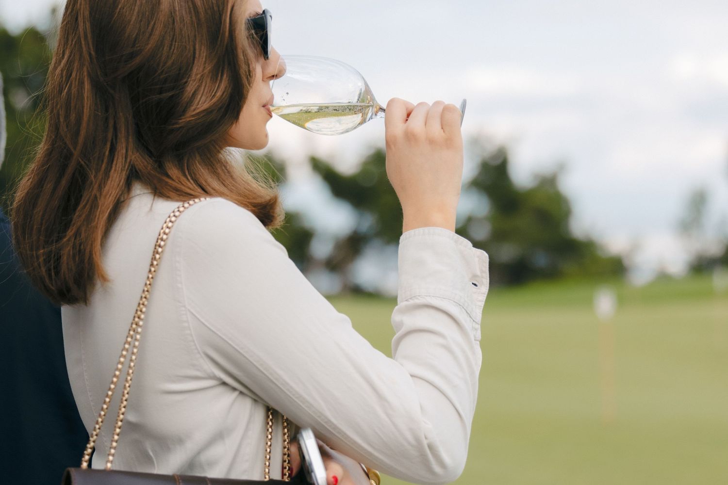 Person holding up a drink glass against a green outdoor background.