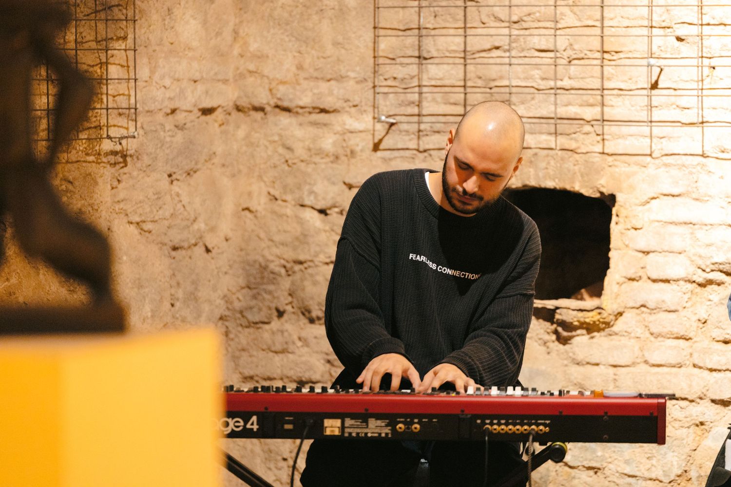 Musician playing a digital piano keyboard in a dimly lit venue.