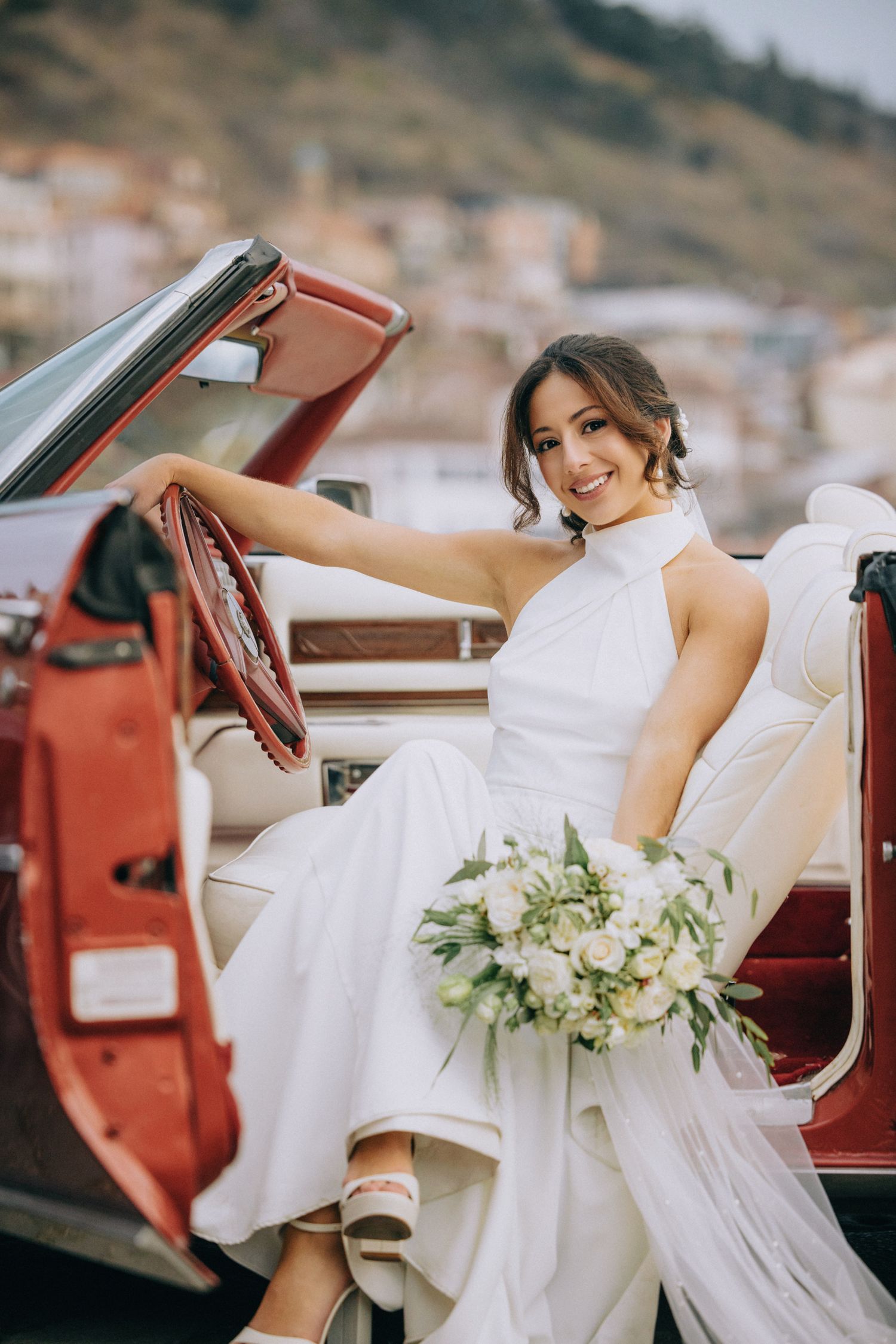 A white wedding dress and bouquet draped elegantly over a classic red convertible car.