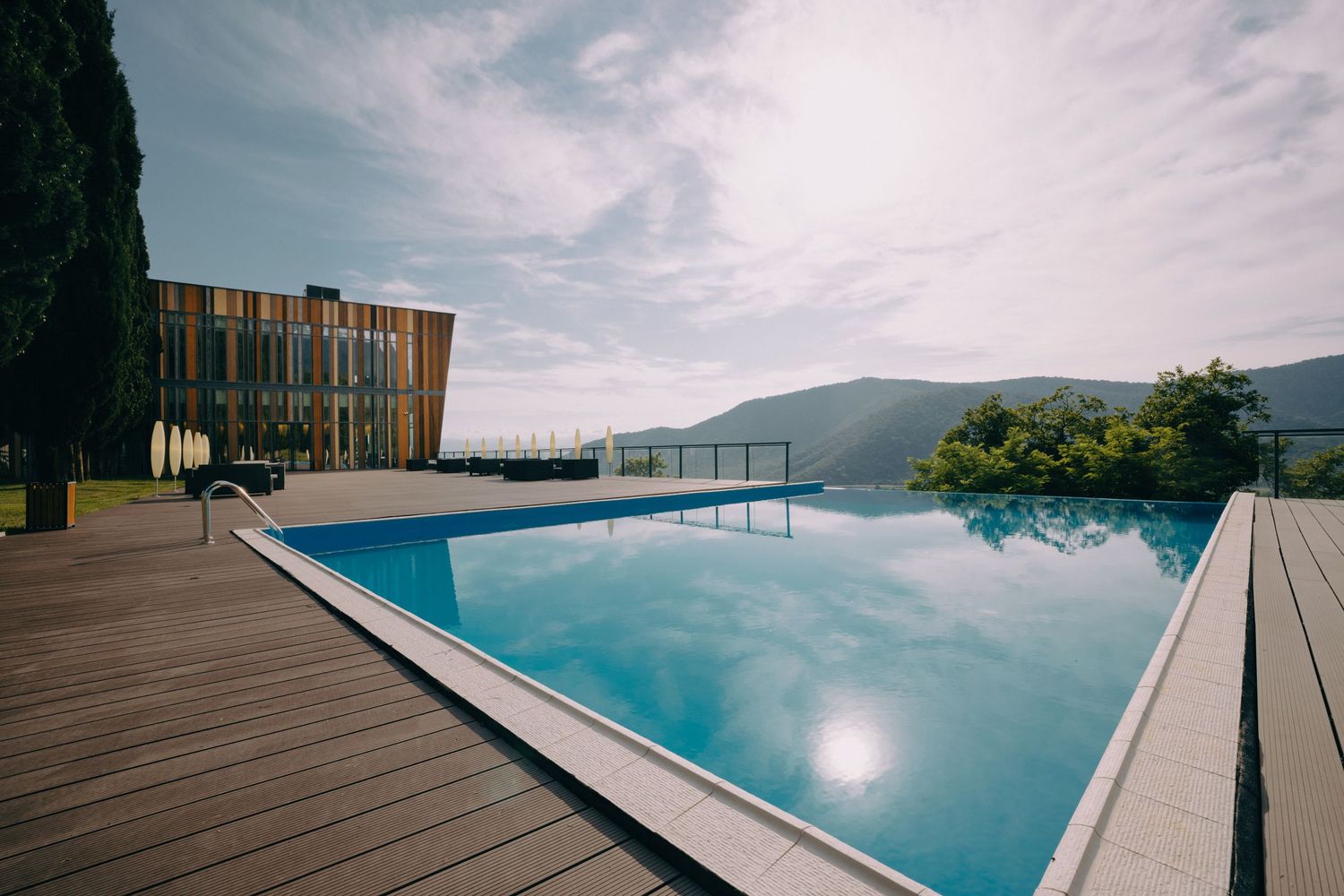 Luxurious infinity pool with wooden deck overlooking mountain landscape and modern architecture.