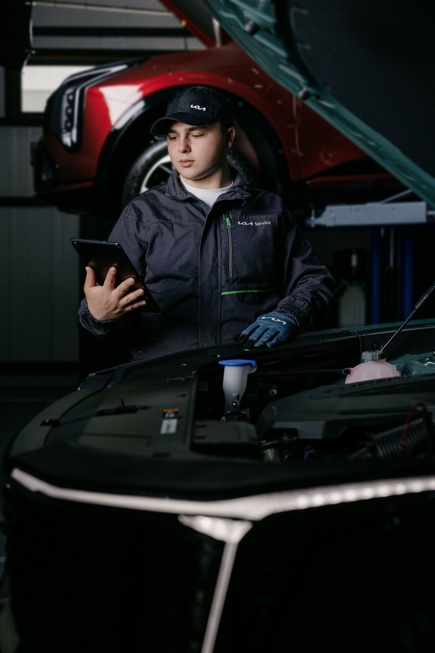 A mechanic in uniform uses a tablet to diagnose a car engine in a professional auto repair shop.