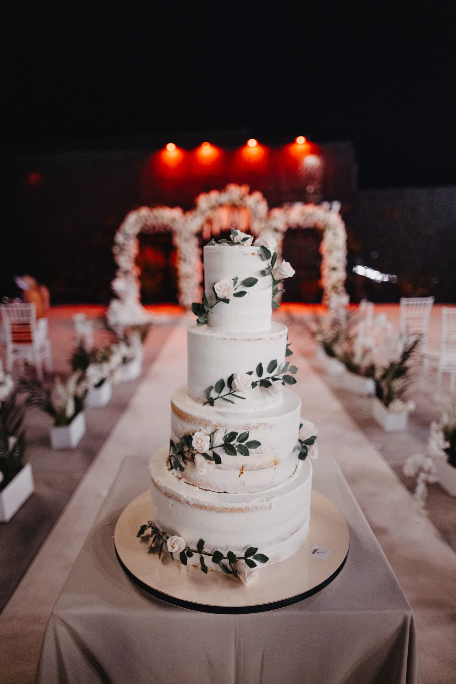Elegant four-tier white wedding cake decorated with delicate black leaf details.