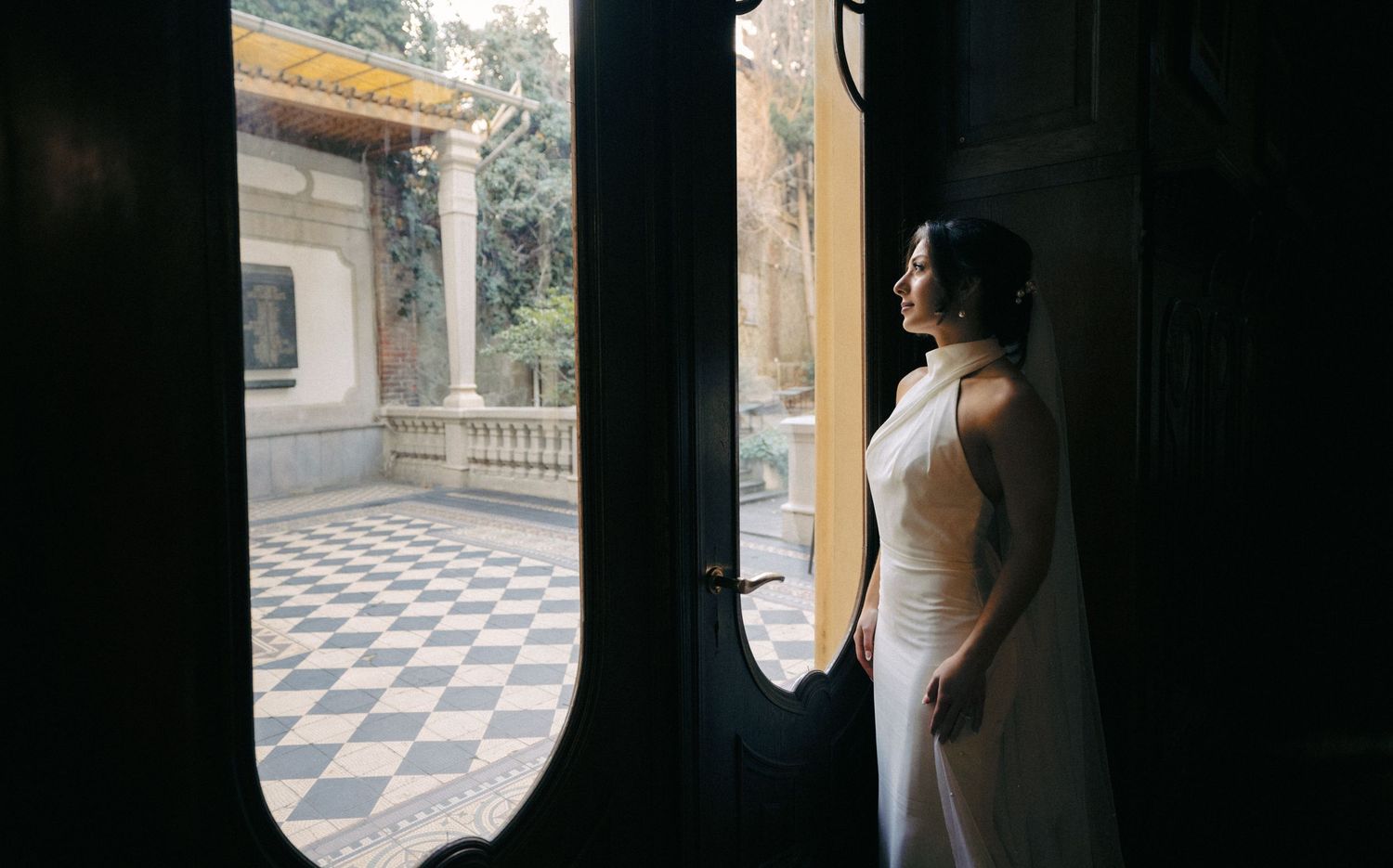 Elegant bride poses in a white gown against a bright window with architectural details.