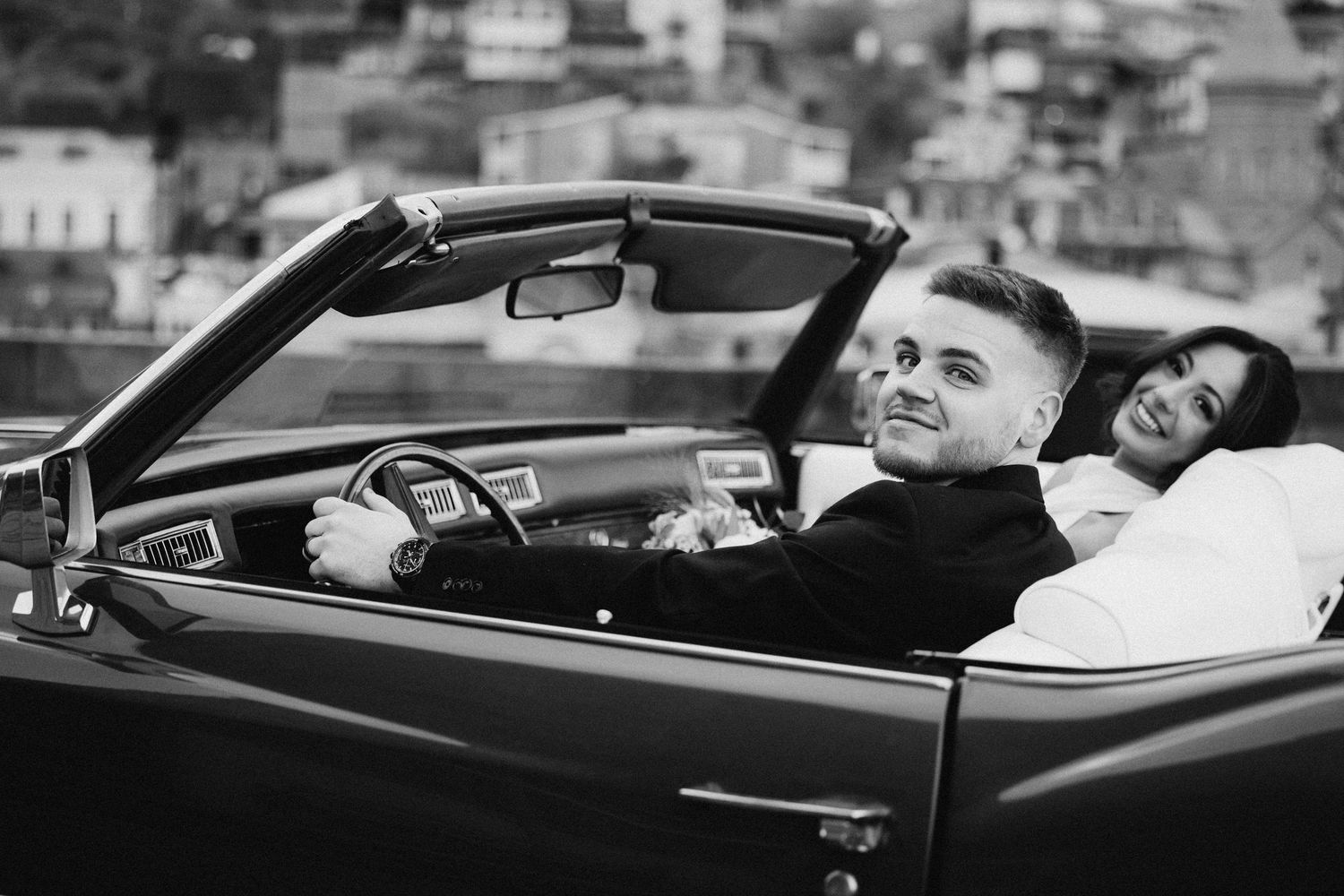 Black and white photo of newlyweds enjoying a ride in vintage convertible.