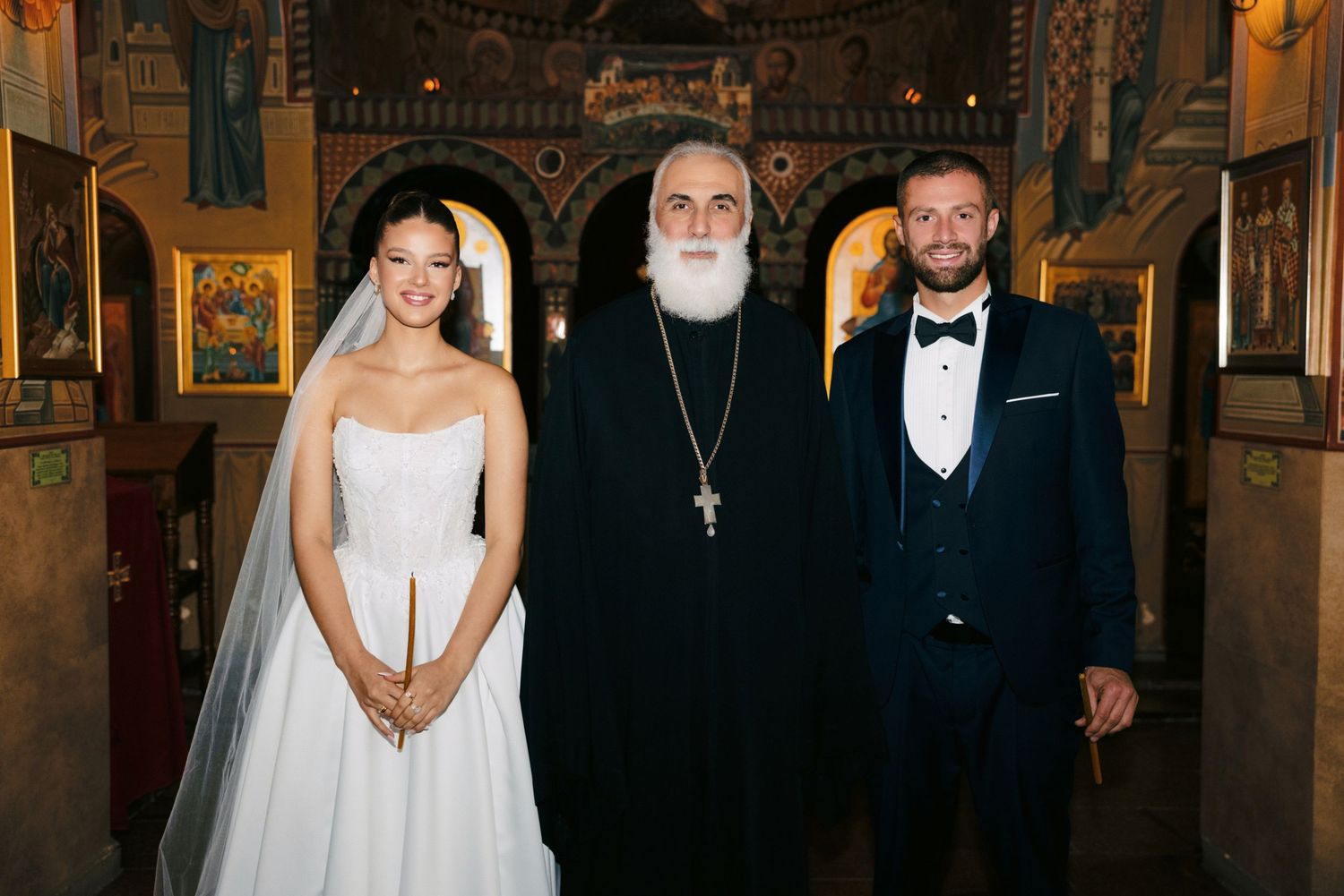 Orthodox wedding ceremony with priest in traditional black robes and ornate church interior.