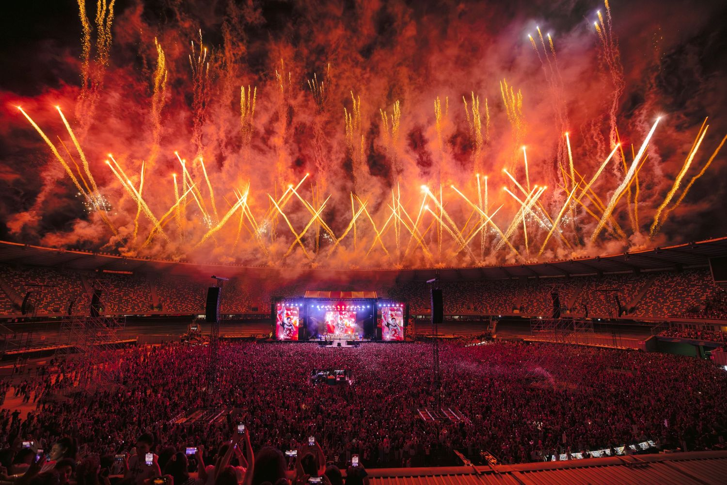 Spectacular fireworks display illuminating stadium with red and gold bursts across night sky.
