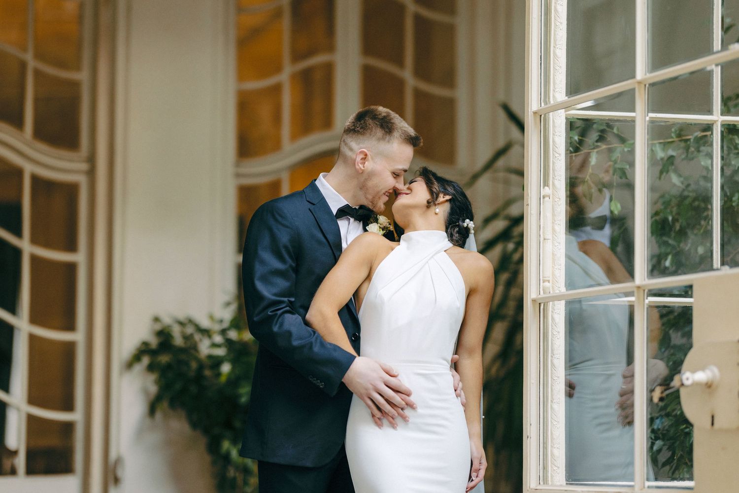 Romantic wedding portrait in elegant room with large windows and indoor plants.