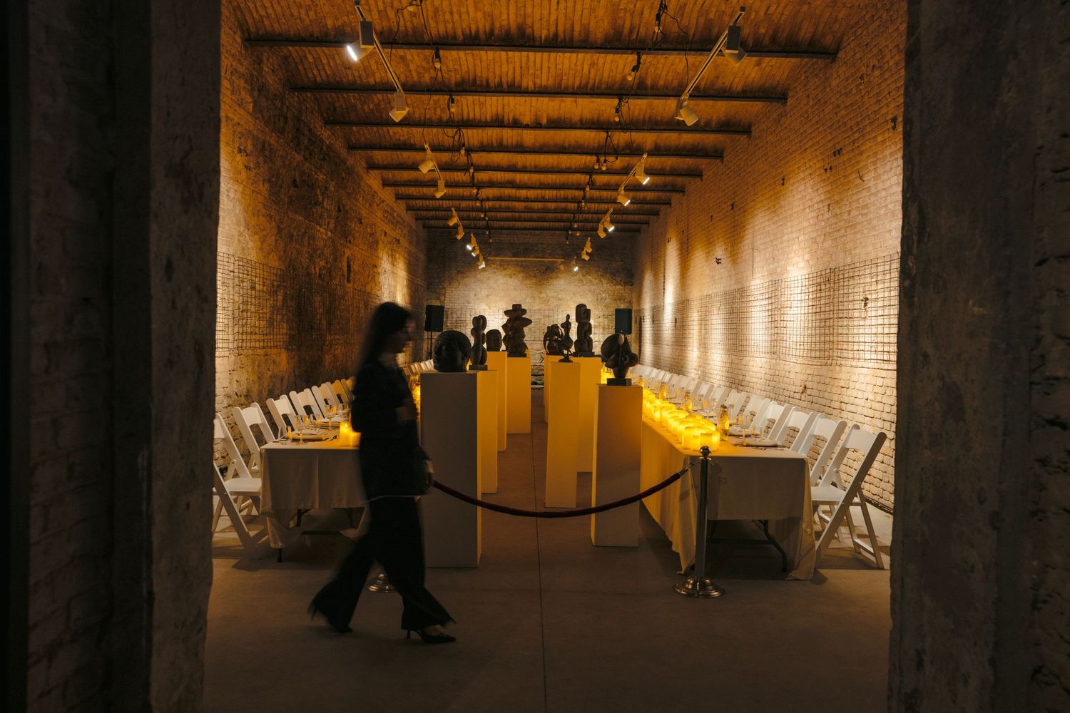 Long underground tunnel with brick walls and dramatic lighting creating silhouettes of people walking.