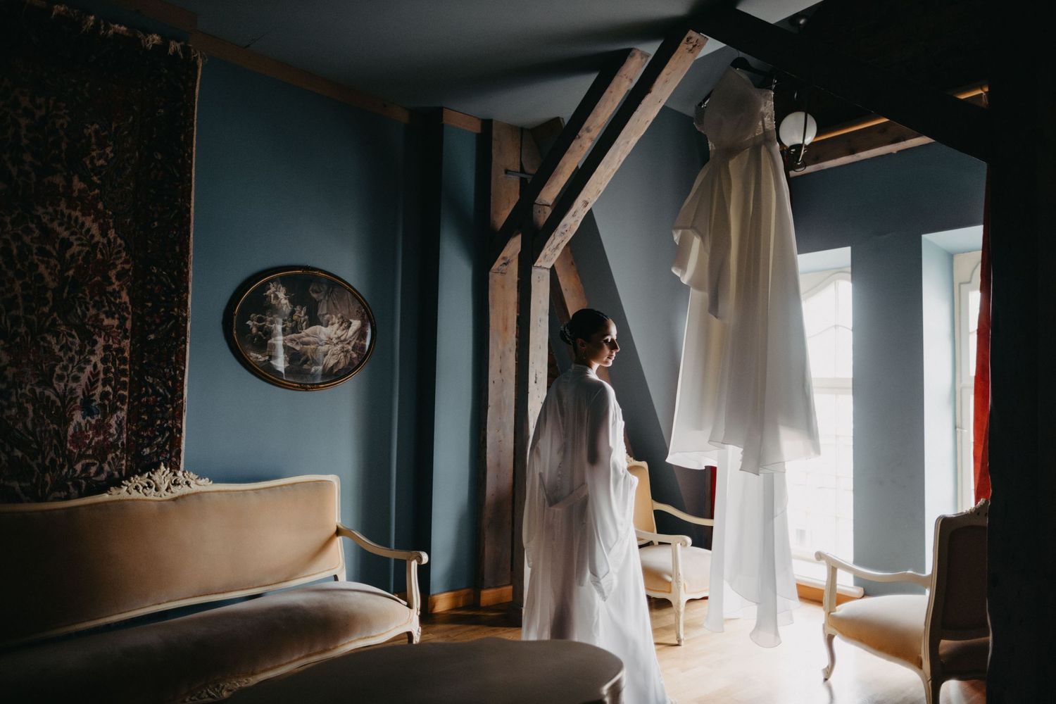 White wedding dress displayed in a blue room with vintage furniture and architectural details.
