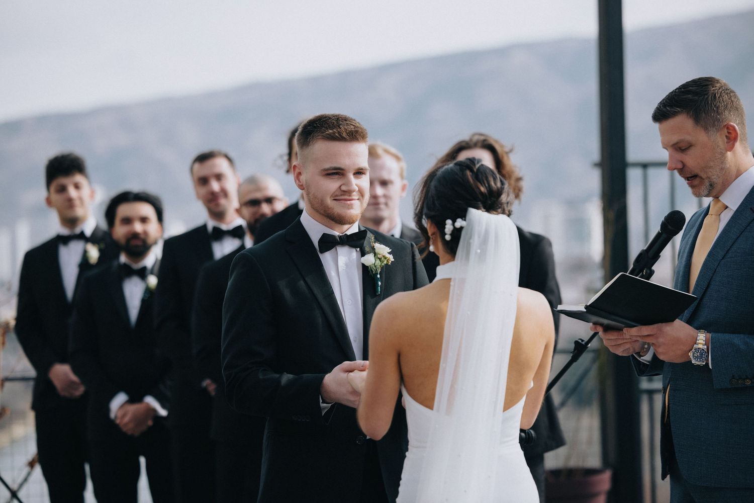 Outdoor wedding ceremony with guests gathered in formal wear against mountain backdrop.