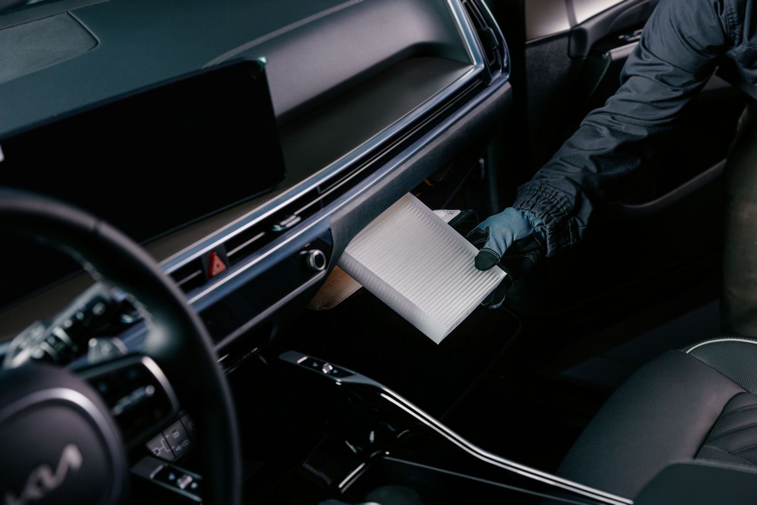 A technician in black gloves replacing a cabin air filter in a Kia vehicle during a professional car detailing service.