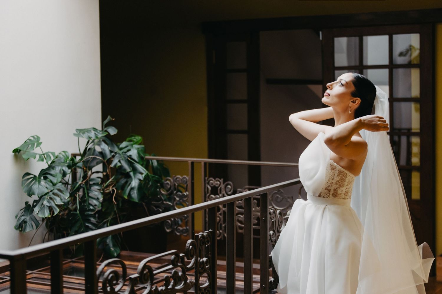 Bride in classic white wedding dress stands gracefully against ornate staircase railing.