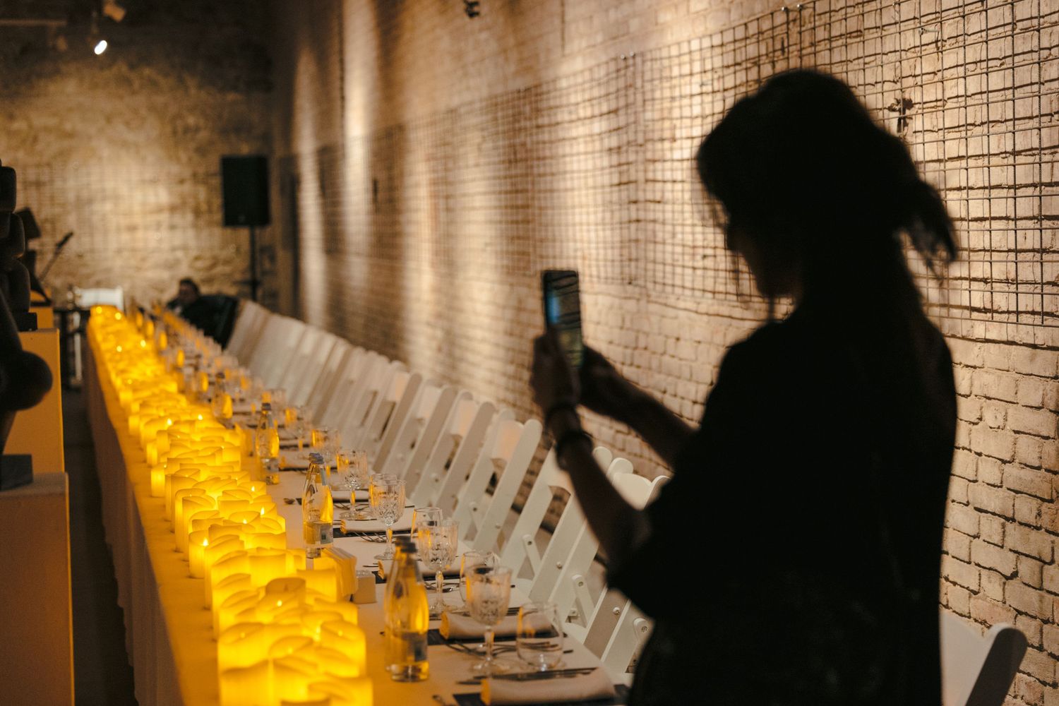 Silhouetted figures viewing illuminated art displays in a brick-walled gallery.