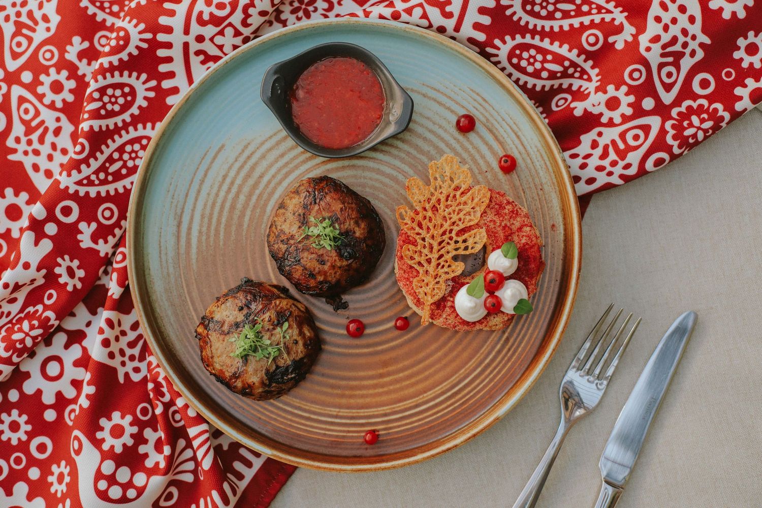 Elegant plated dishes on red and white patterned tablecloth with artistic presentation.