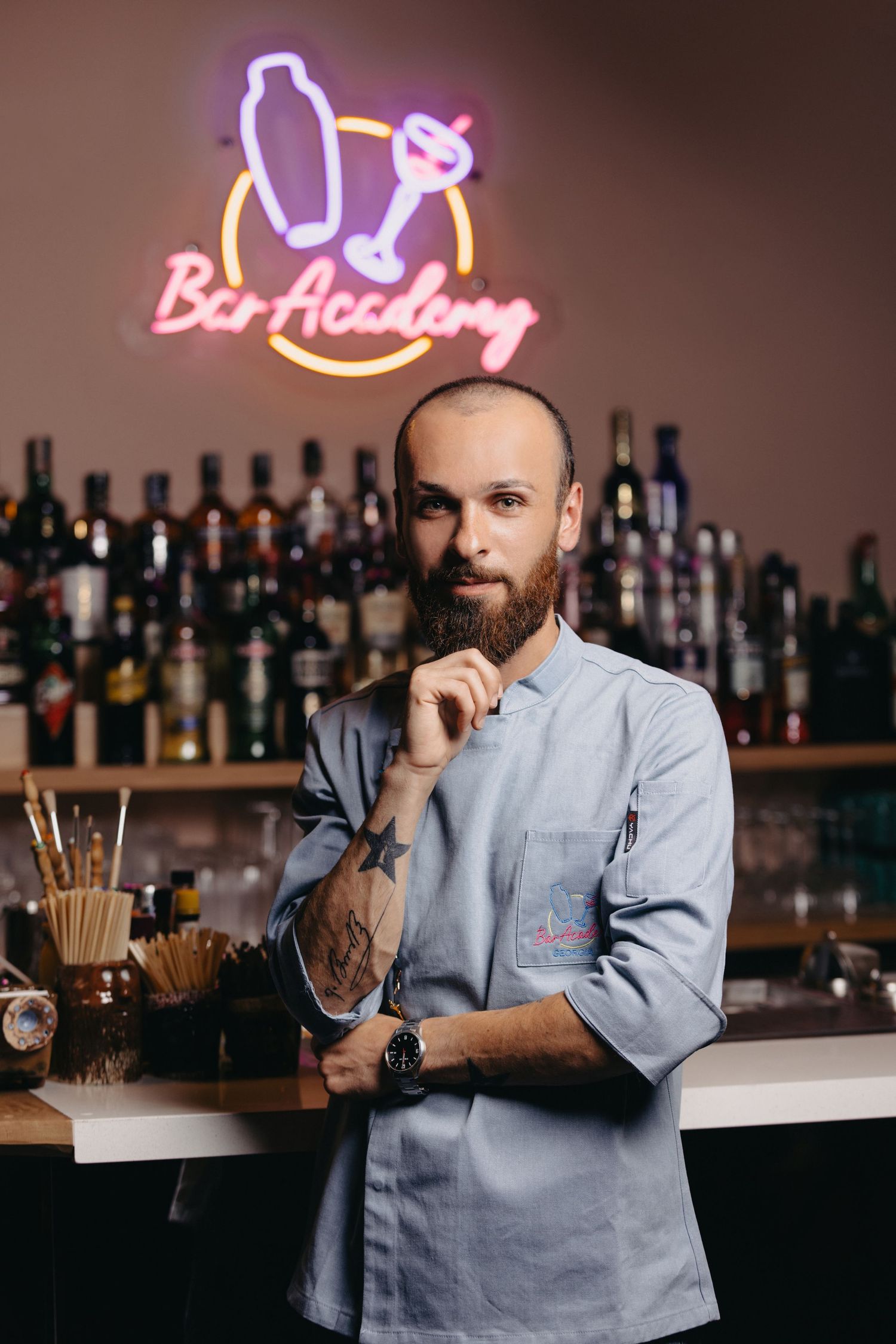 Bartender in grey uniform working behind bar counter with neon signage.