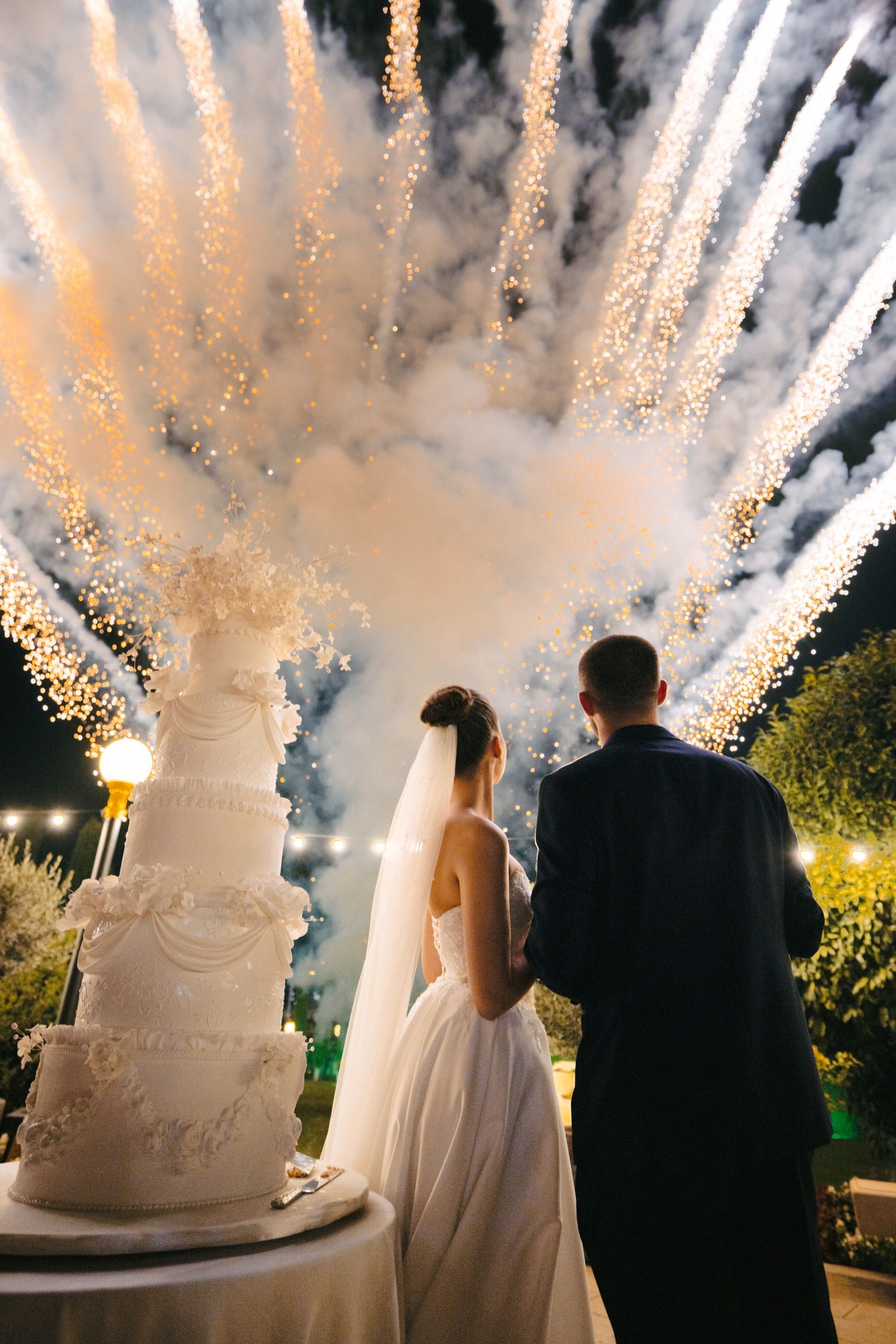 Wedding cake display with dramatic sparkler fountains creating a shower of golden light.