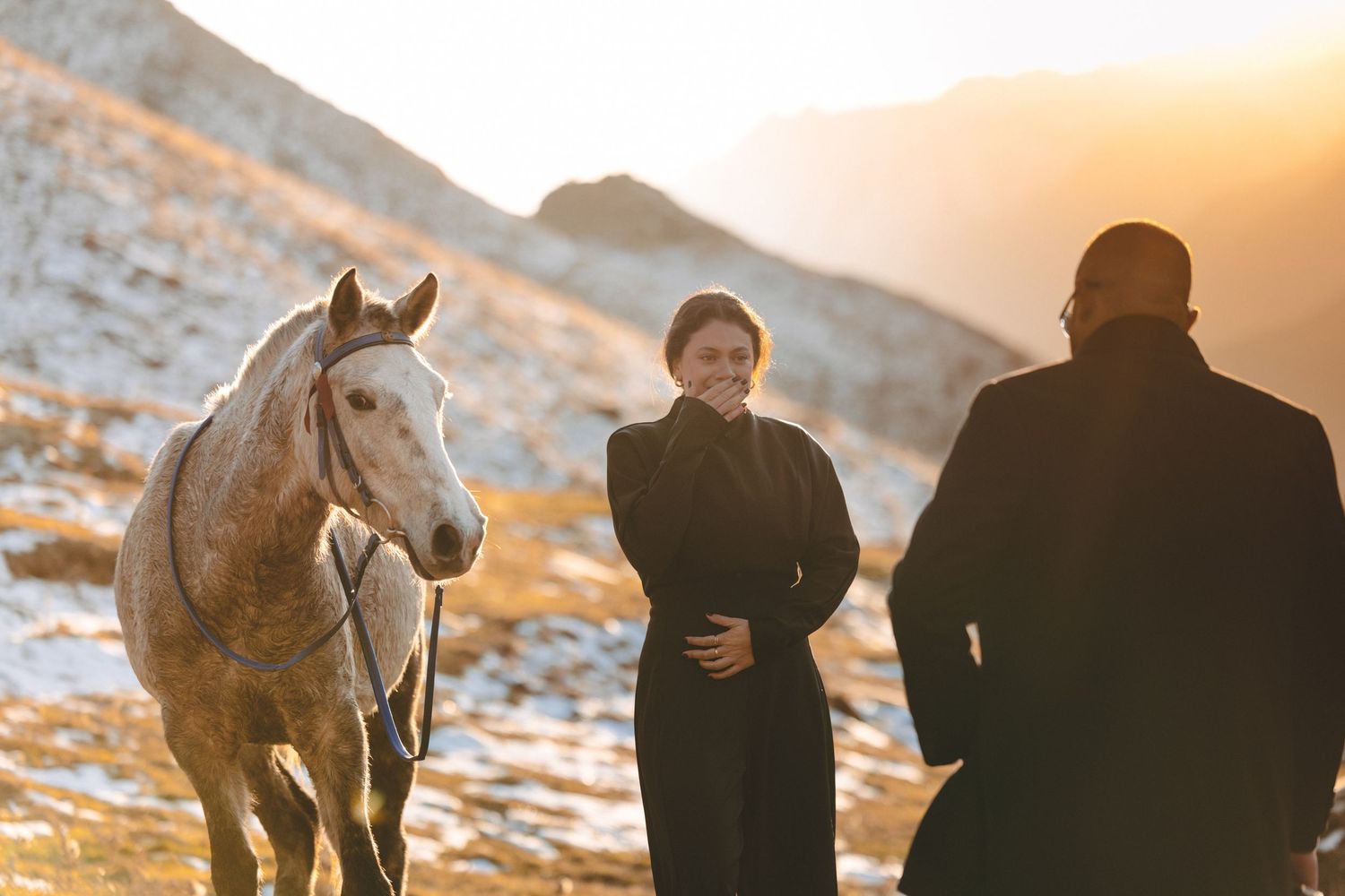 White horse stands in snowy mountain landscape during golden hour.