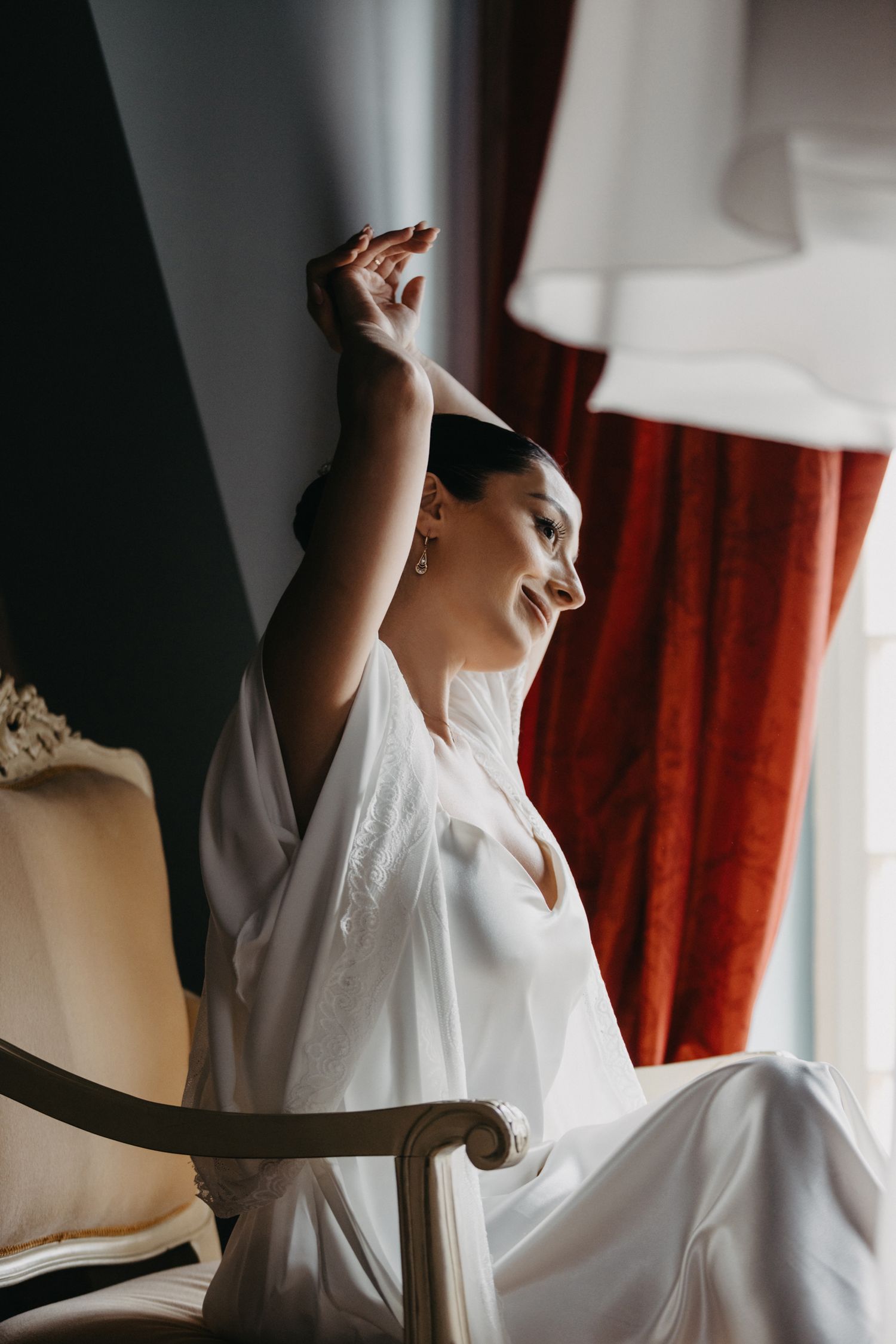 Person in white robe sitting in vintage chair with natural light streaming through window.