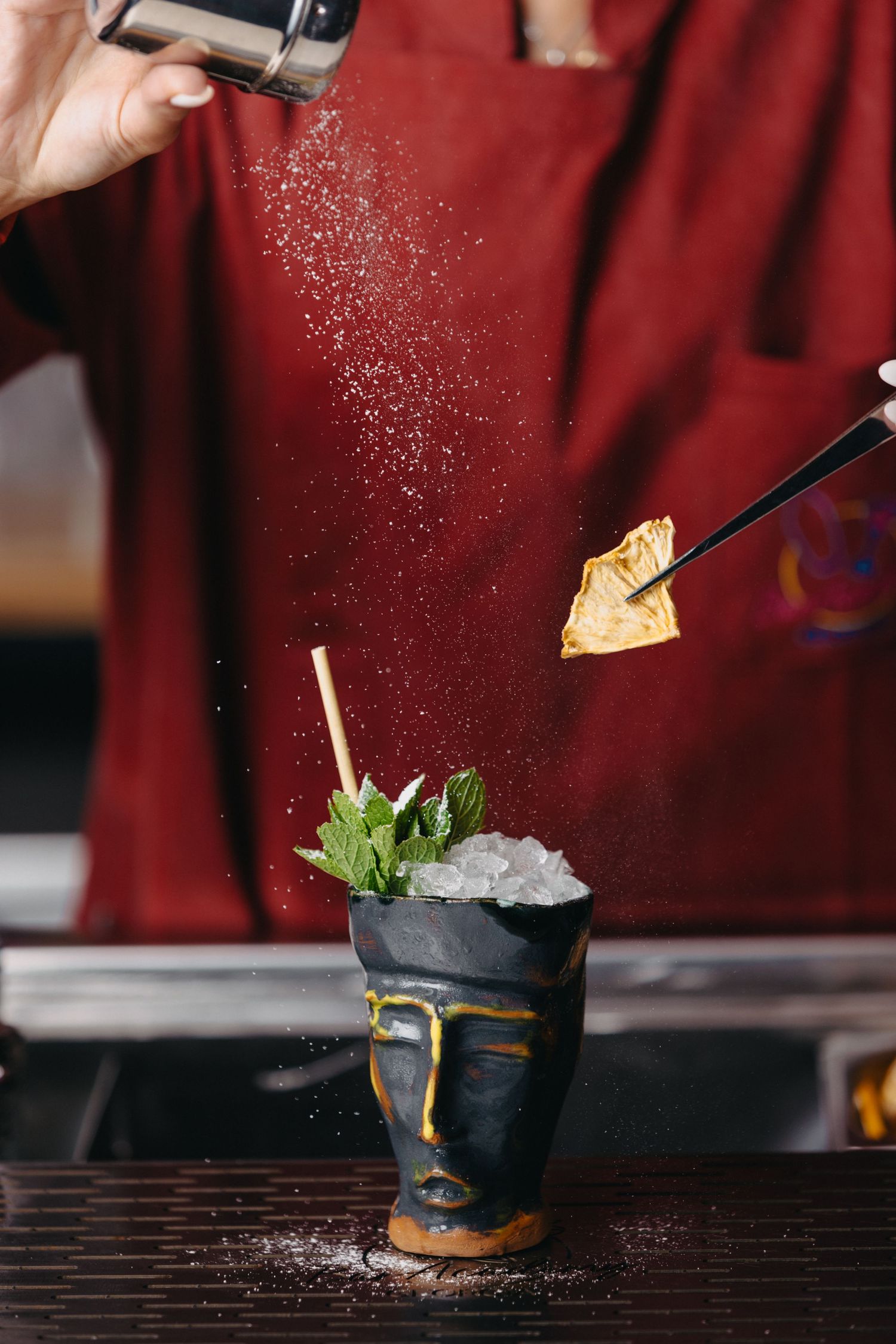 Bartender sprinkles garnish on a cocktail with a dark background and neon lighting.