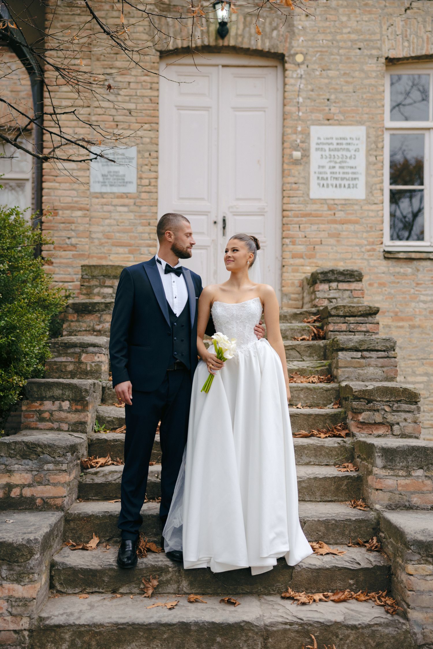 Elegant couple shares joyful moment on stone steps of historic brick building.