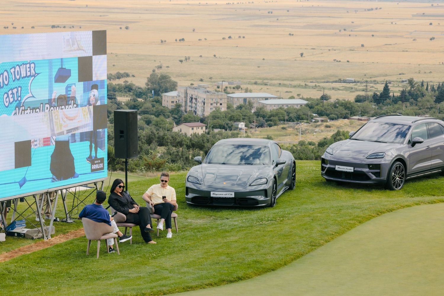 Luxury cars parked on grass with promotional banners in the background.