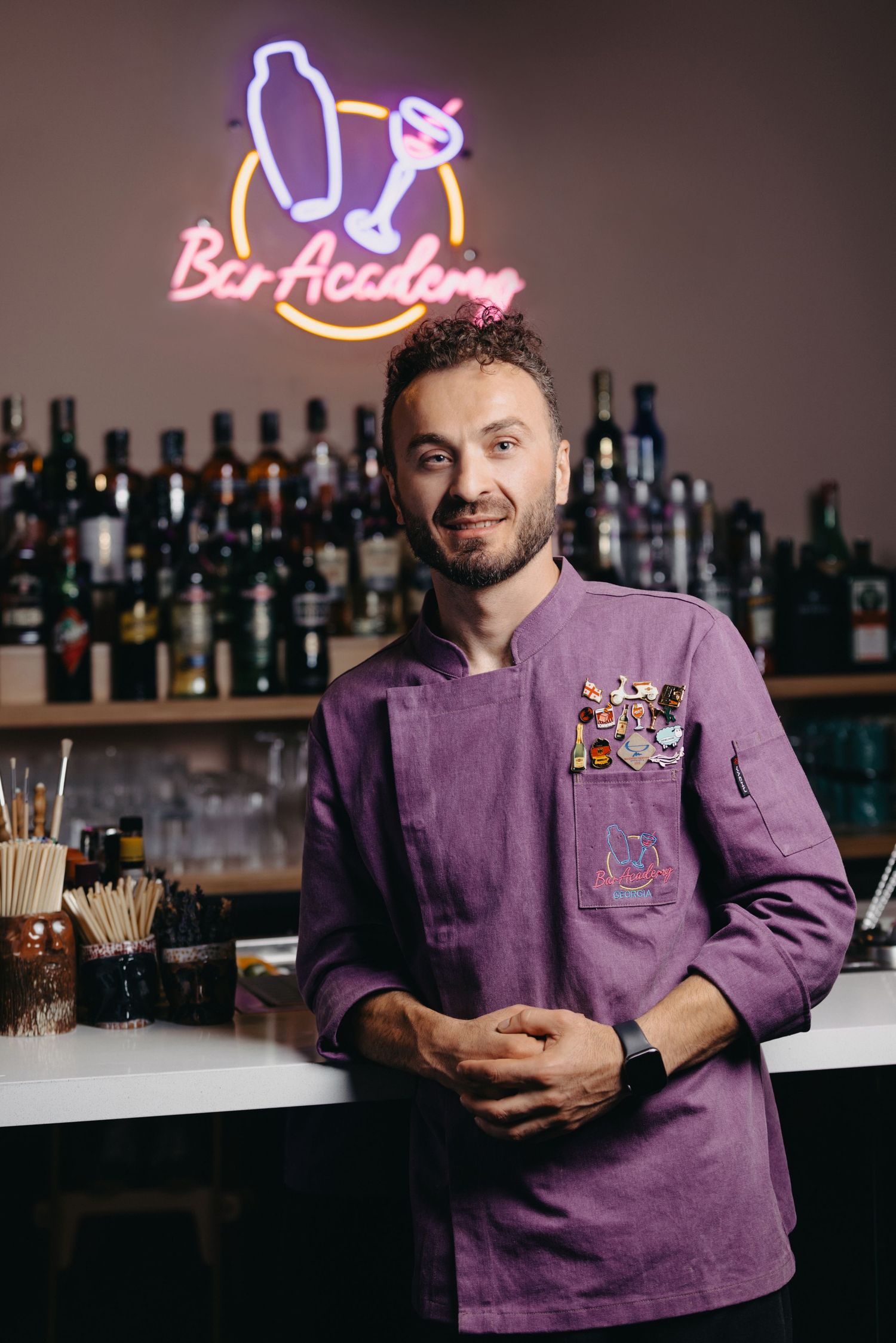 Mixologist in purple uniform serving drinks at bar with neon lighting.