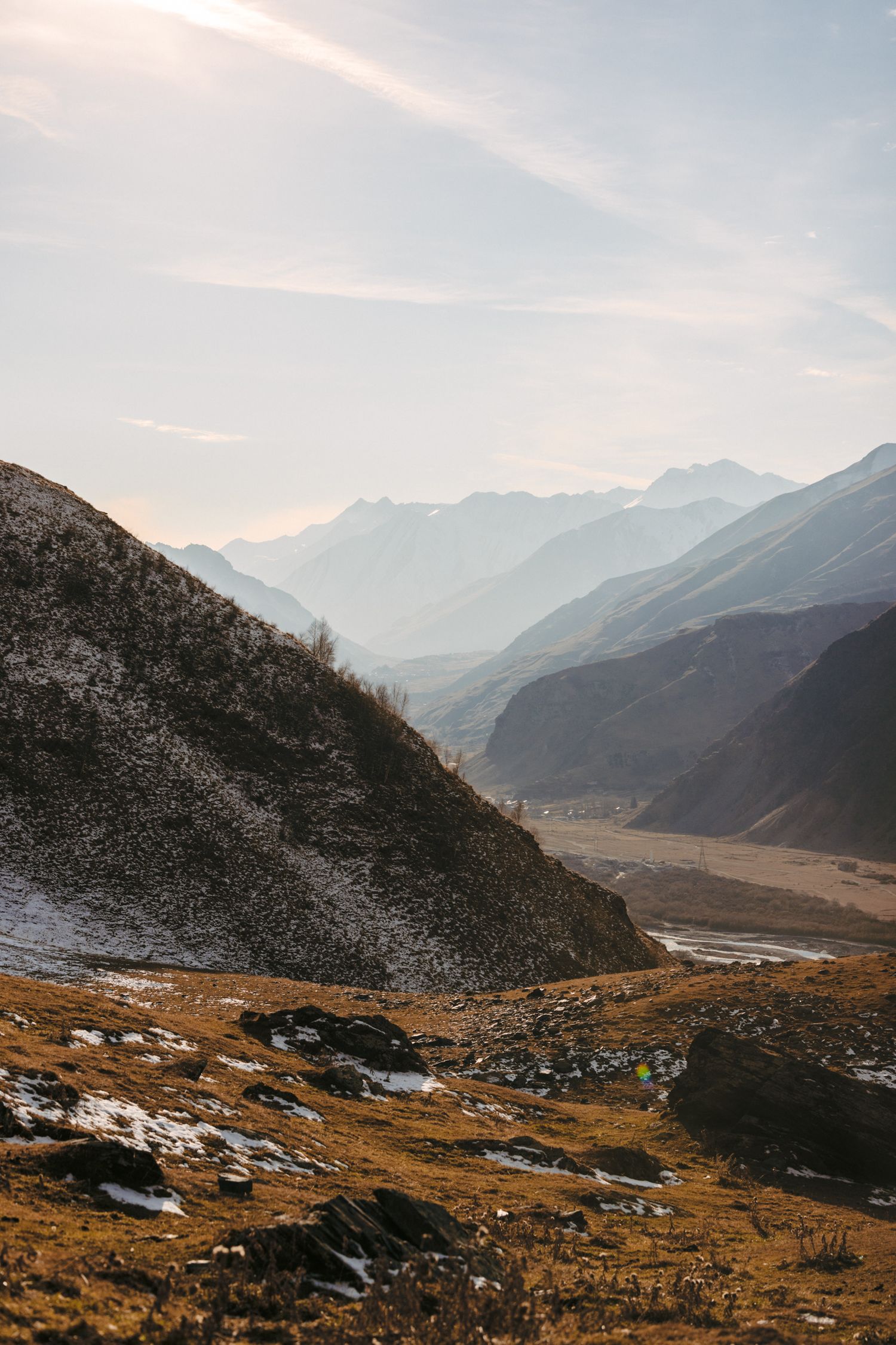 Snow-dusted mountain valley with autumn colors and distant peaks under cloudy sky.