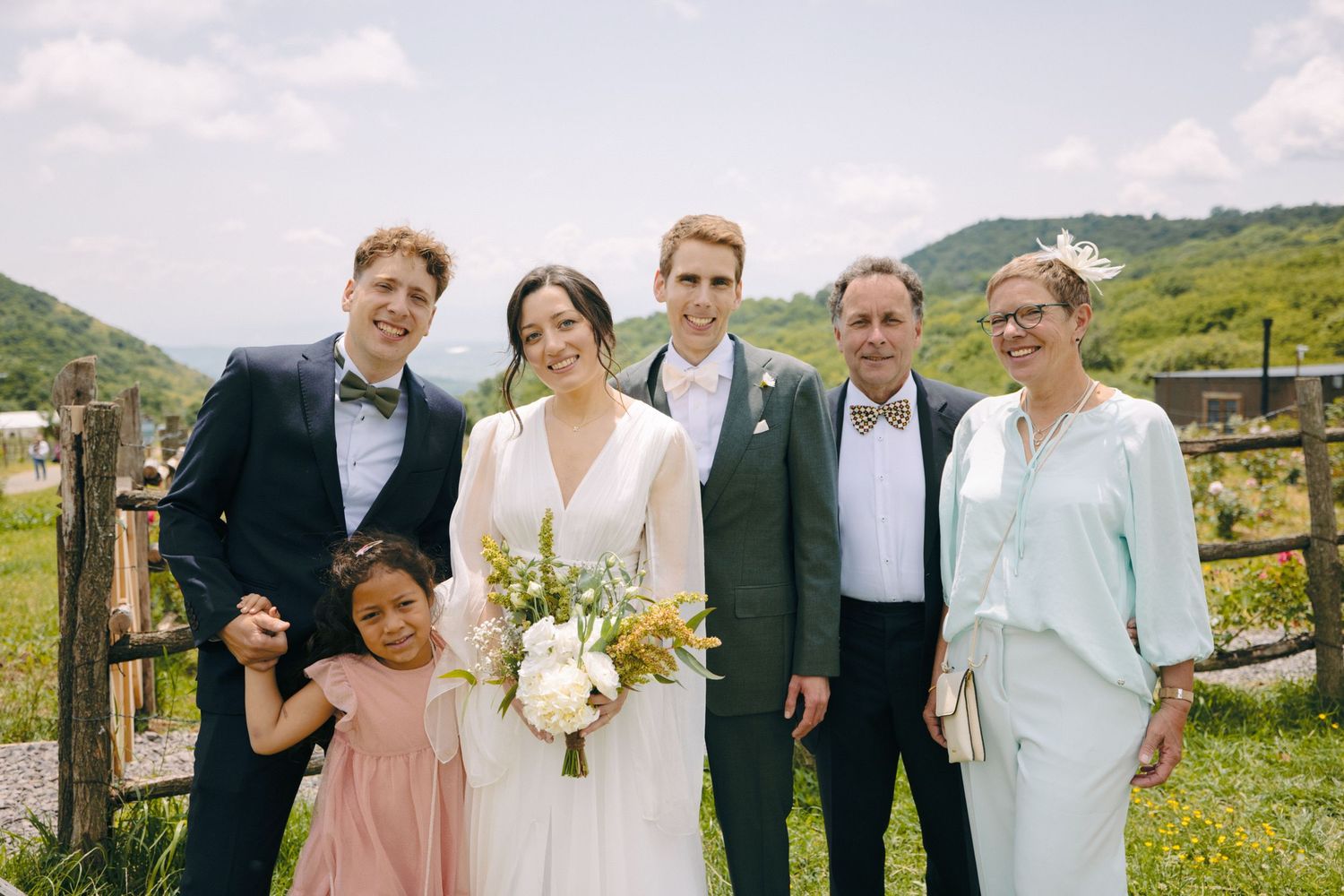 Wedding party posing together outdoors with mountains in the background.