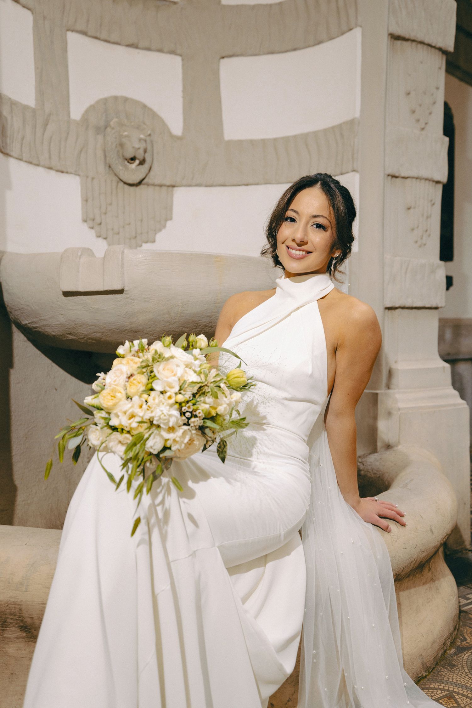Bride in high-neck white gown holds cream and white floral bouquet.