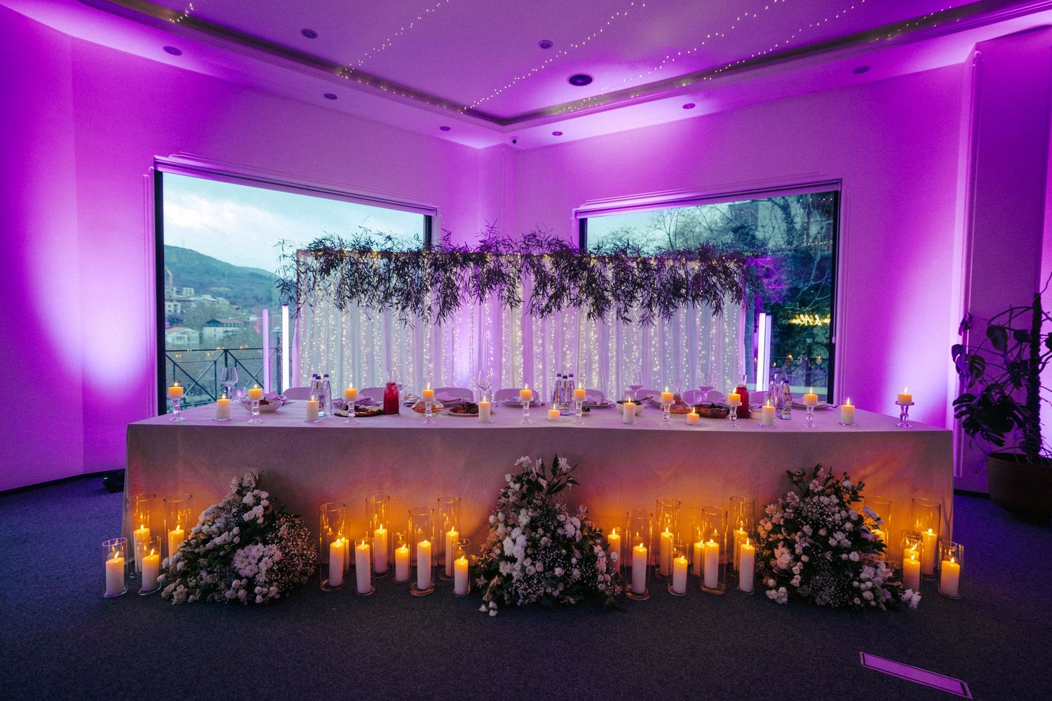 Purple-lit wedding reception venue with elegant floral decorations and ambient lighting.