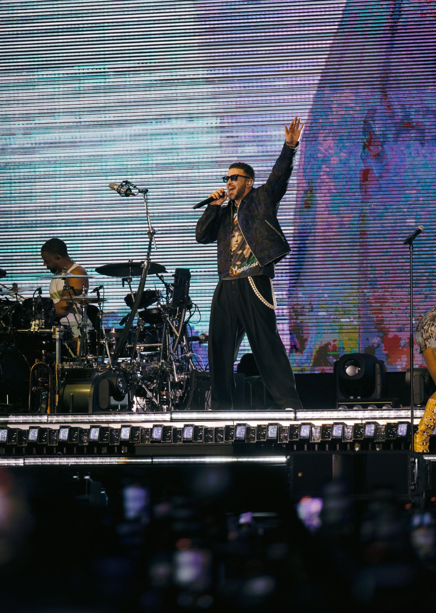 Performer on stage with dramatic lighting and video screen backdrop during stadium concert.