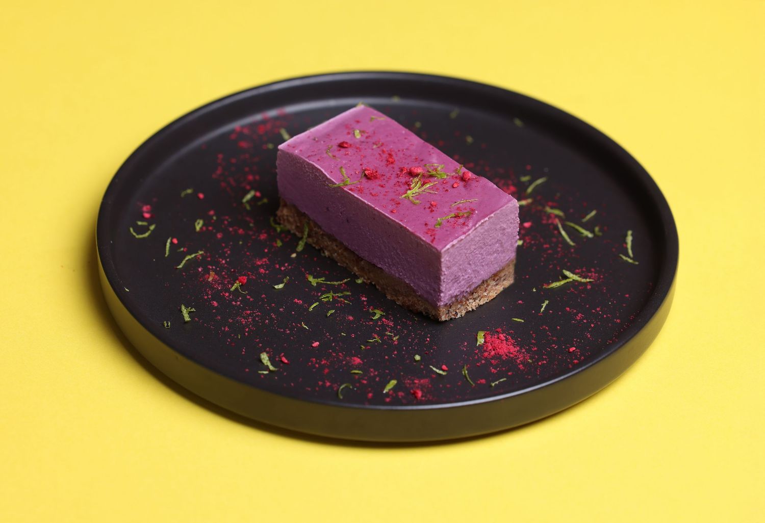 Purple dessert bar on a black plate against vibrant yellow background with colorful sprinkles.