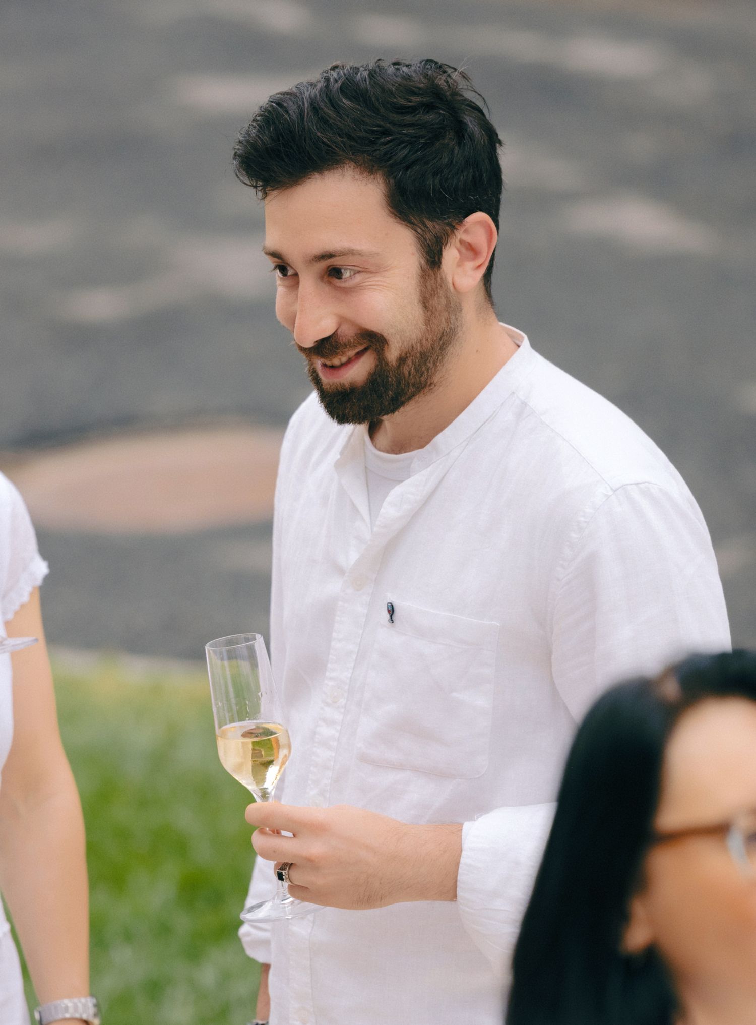 Guest in white attire enjoying champagne at an outdoor social event.