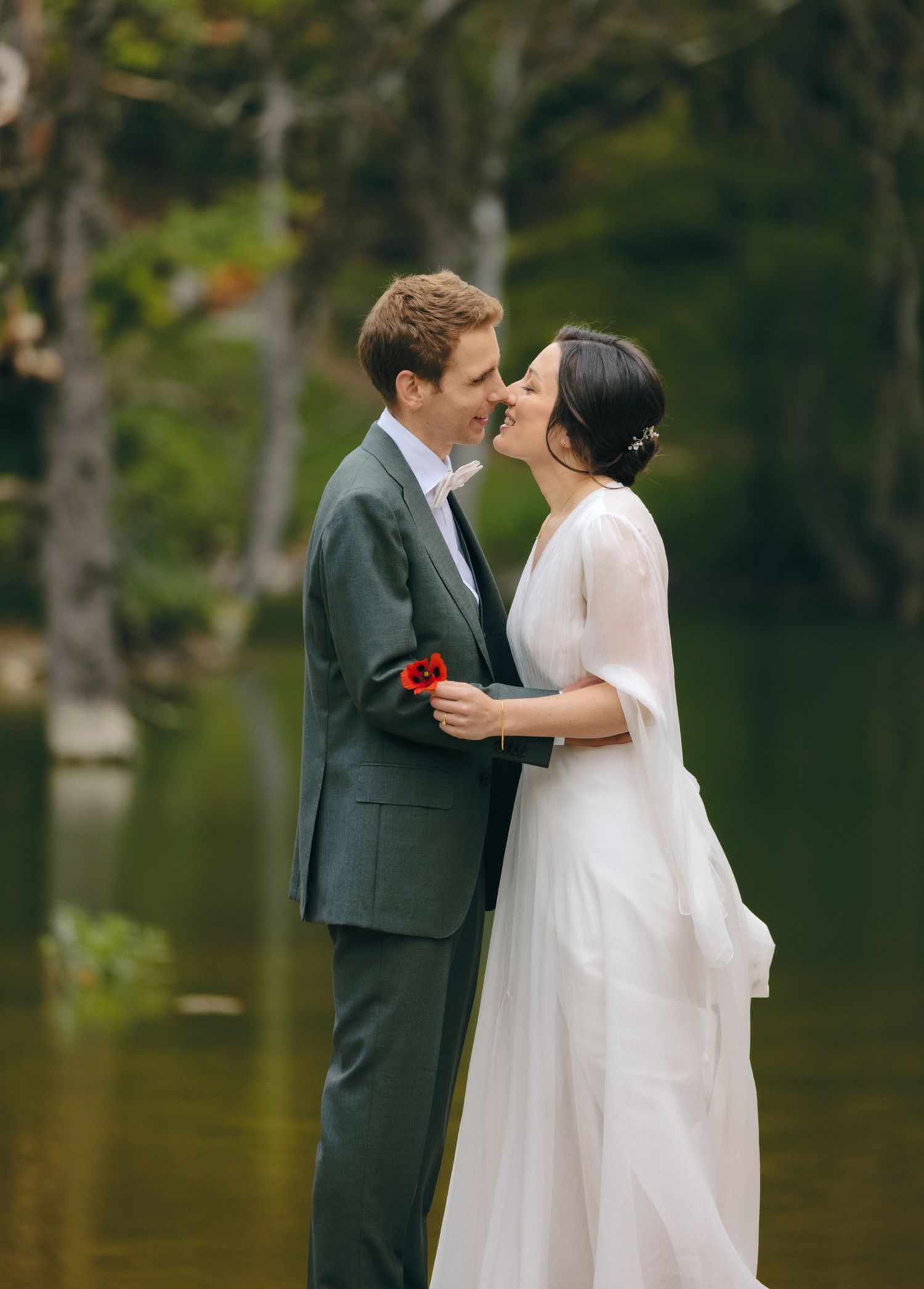 Romantic lakeside moment with couple in formal attire by serene forest waters.