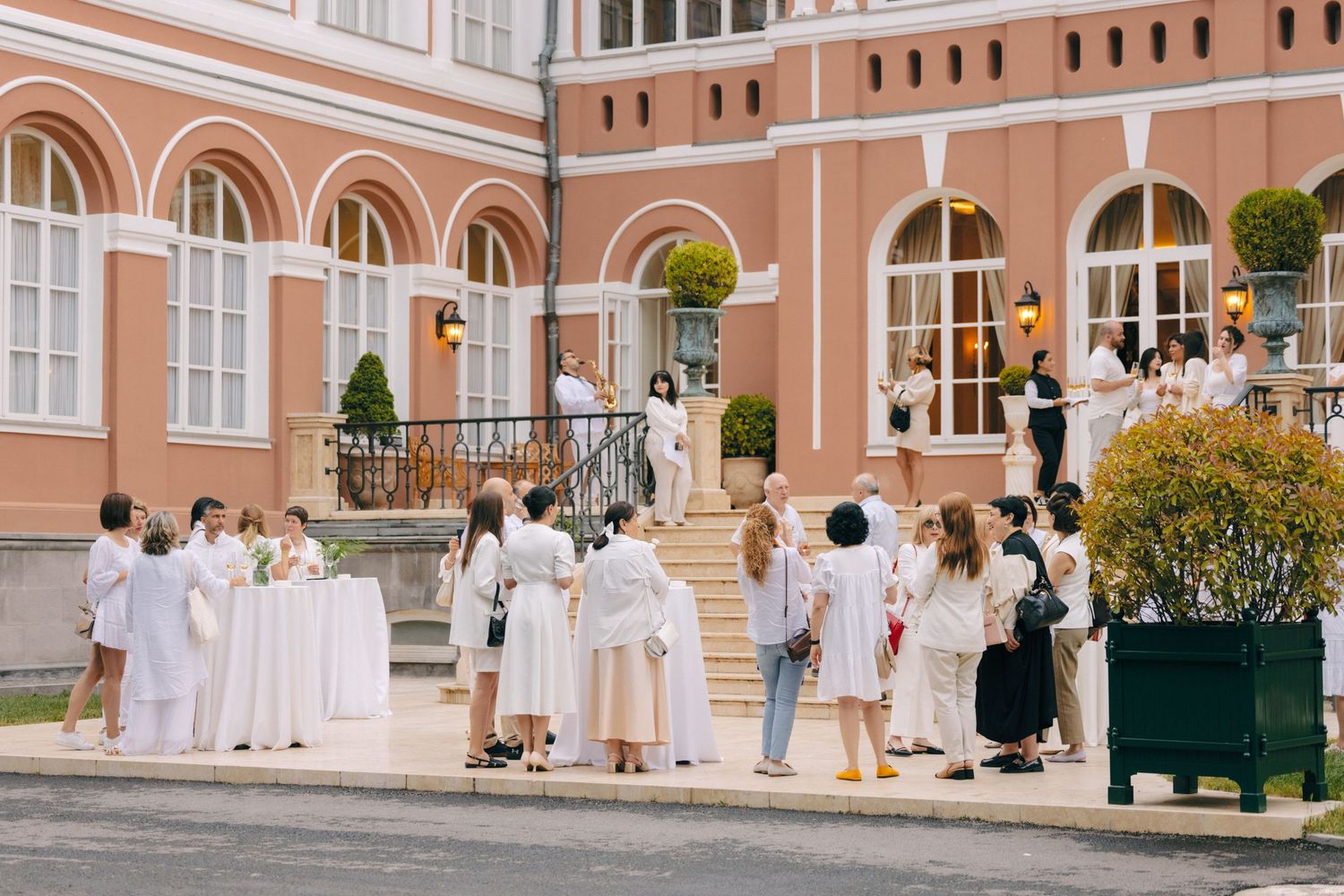 Elegant peach-colored building facade with arched windows hosting outdoor gathering.