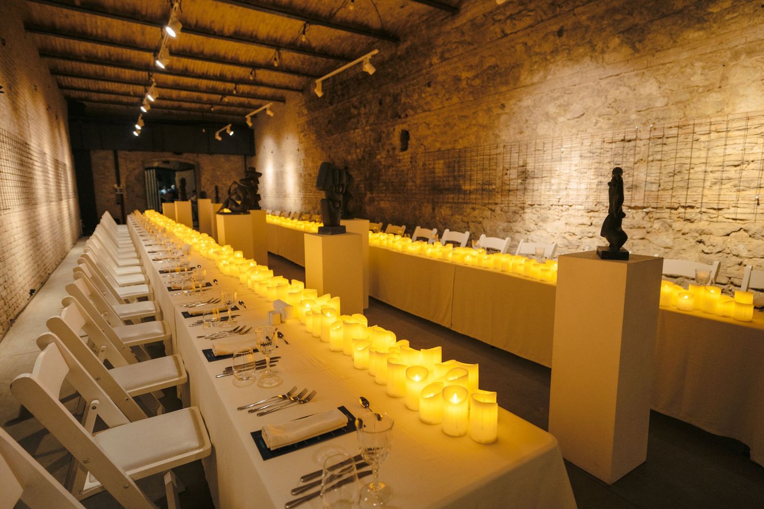Exhibition space with illuminated yellow pedestals displaying artwork along brick walls.