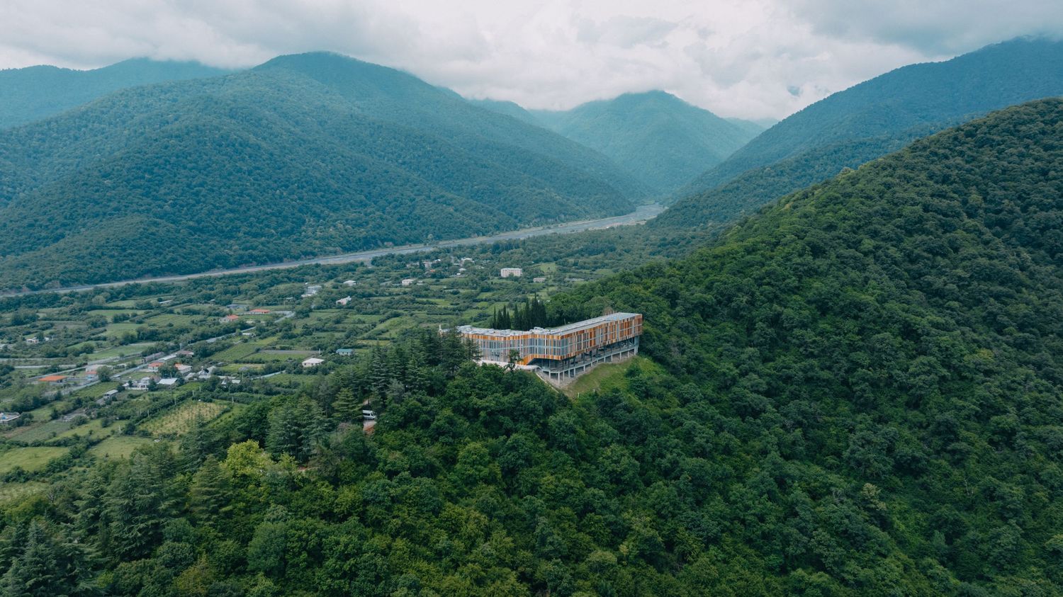 Panoramic mountain range view with lush green valleys and distant buildings nestled in the landscape.
