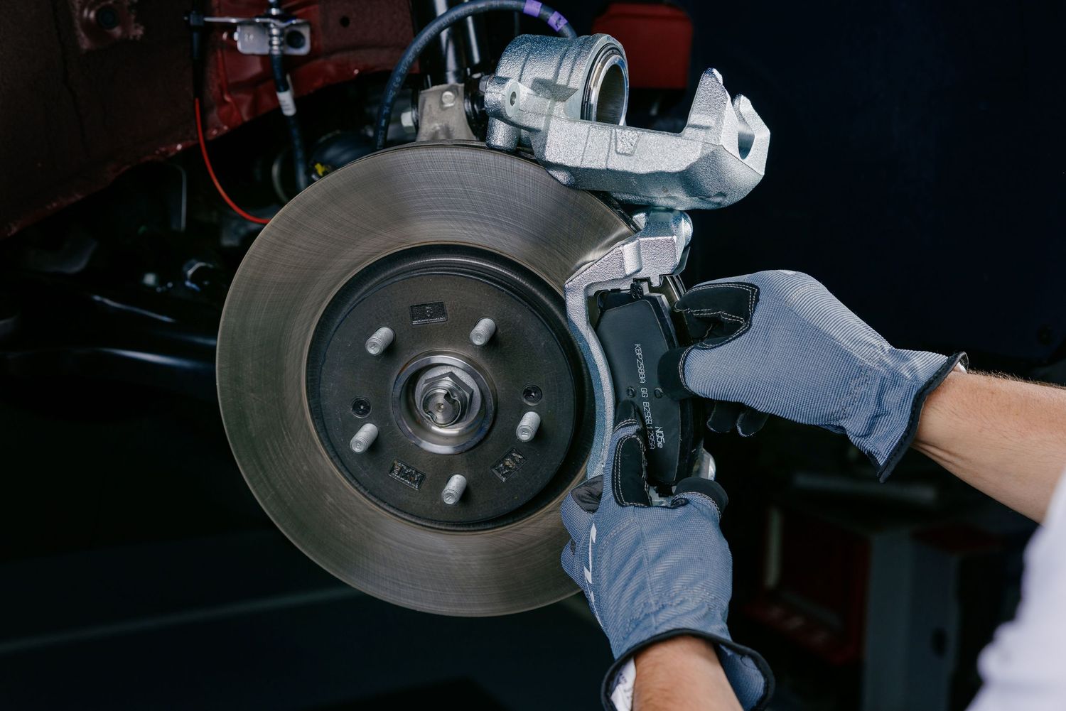 Mechanic in gray gloves replacing disc brake rotor and brake pads on a vehicle during professional auto repair service.