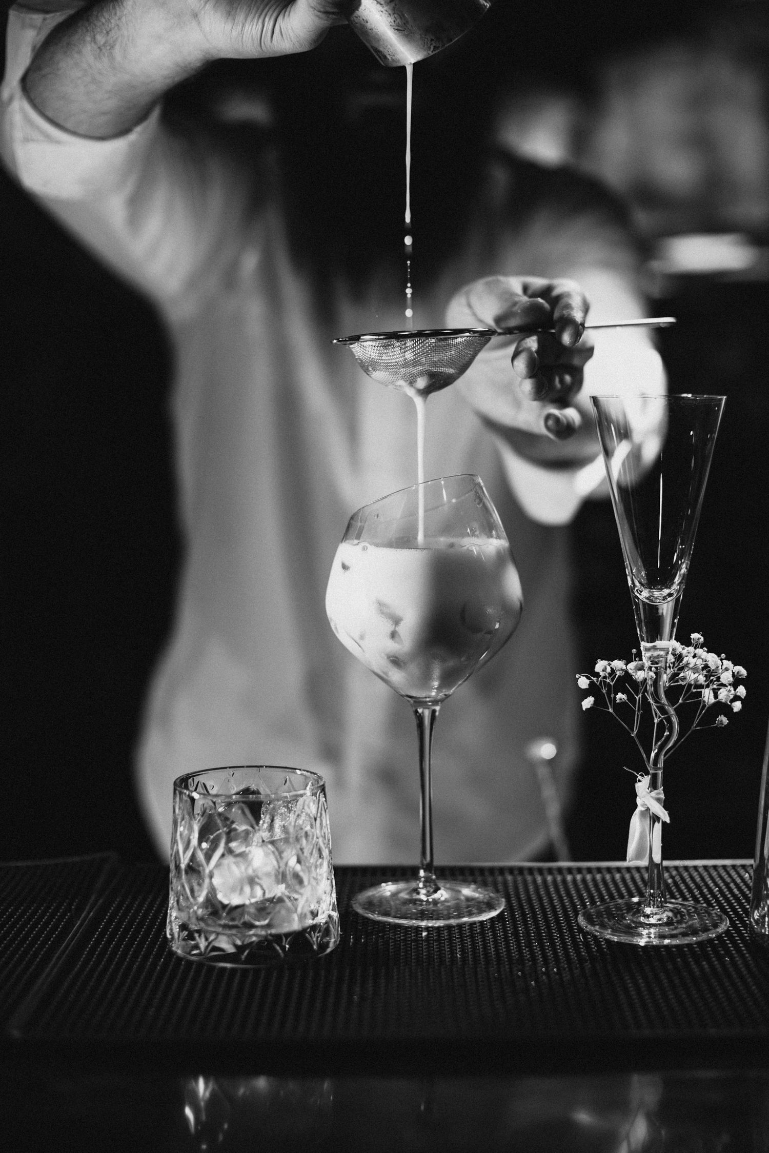 Black and white photograph of cocktail glasses on a bar counter with dramatic lighting.