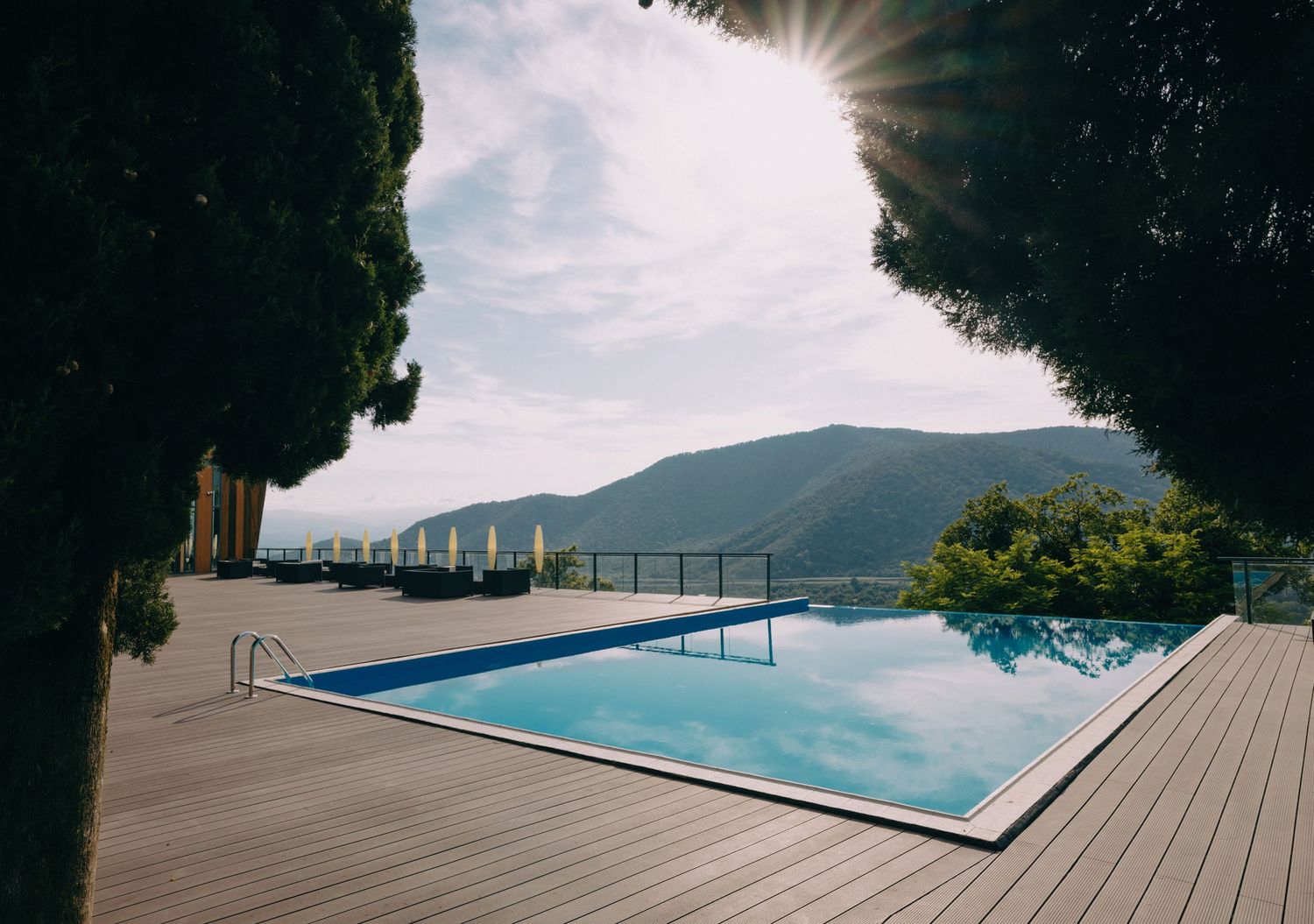 Panoramic view of an outdoor swimming pool with wooden decking and mountain backdrop.