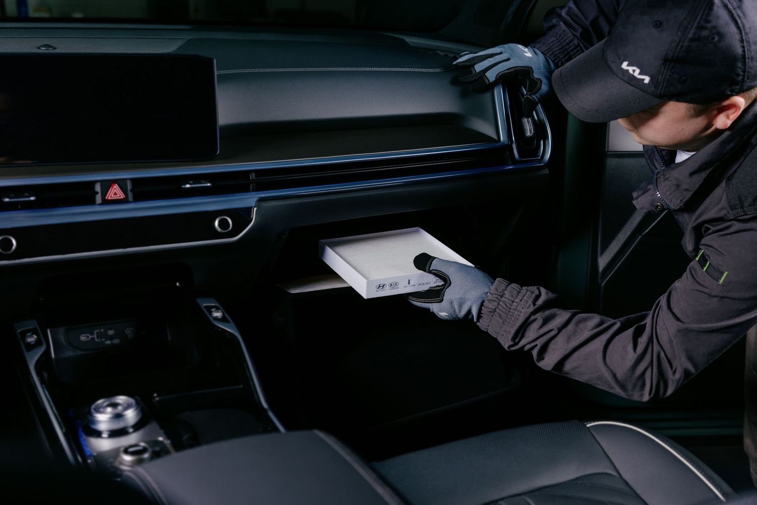 Technician in cap installs cabin air filter into car glove compartment during vehicle maintenance service.
