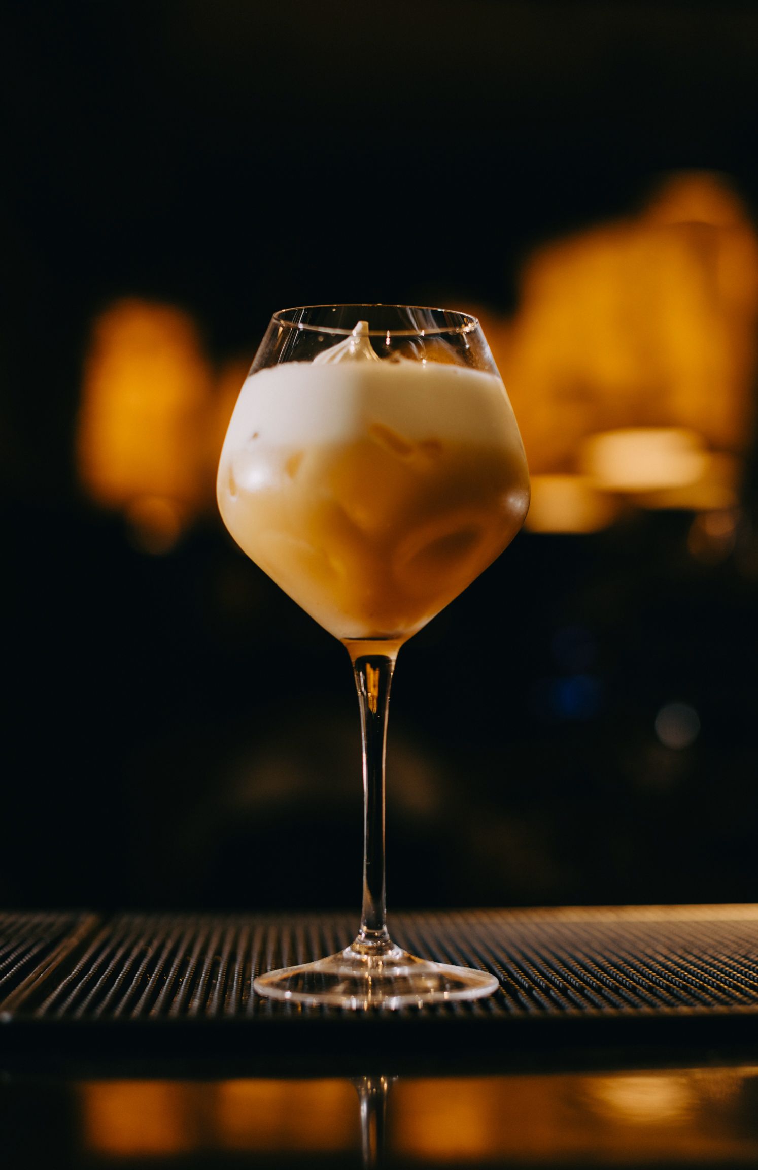 Elegant cocktail glasses with frothy drinks on a dark bar counter in moody lighting.