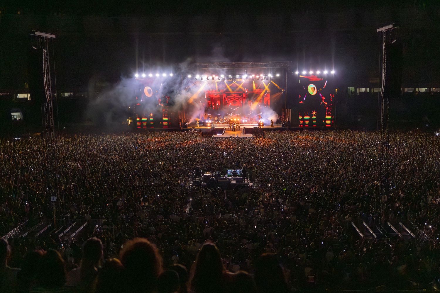 Large outdoor concert venue with bright stage lights and dense crowd of spectators.