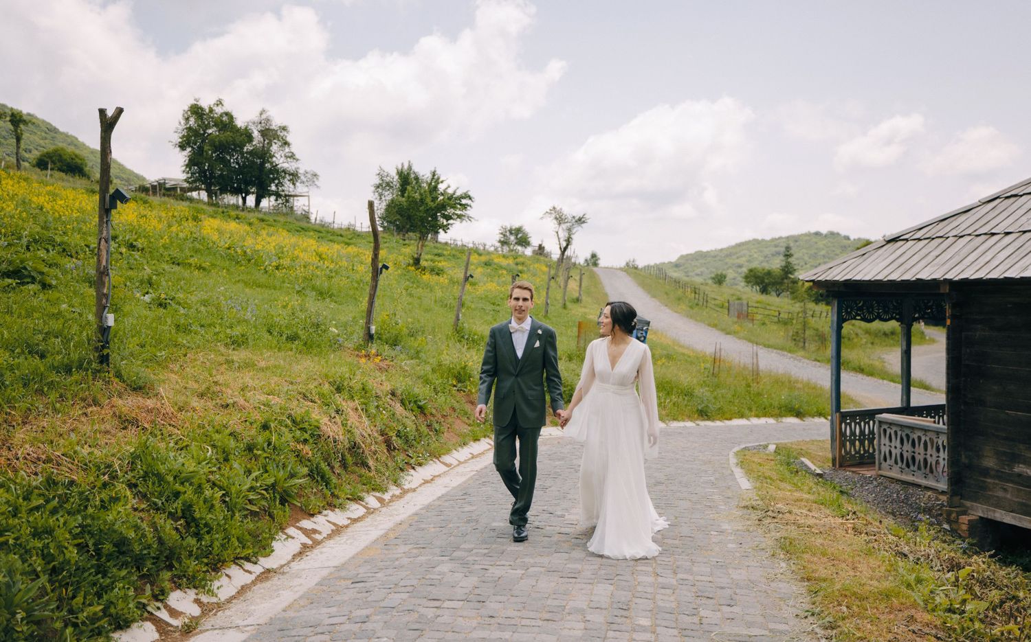 A couple walking along a winding path surrounded by green hills on their wedding day.